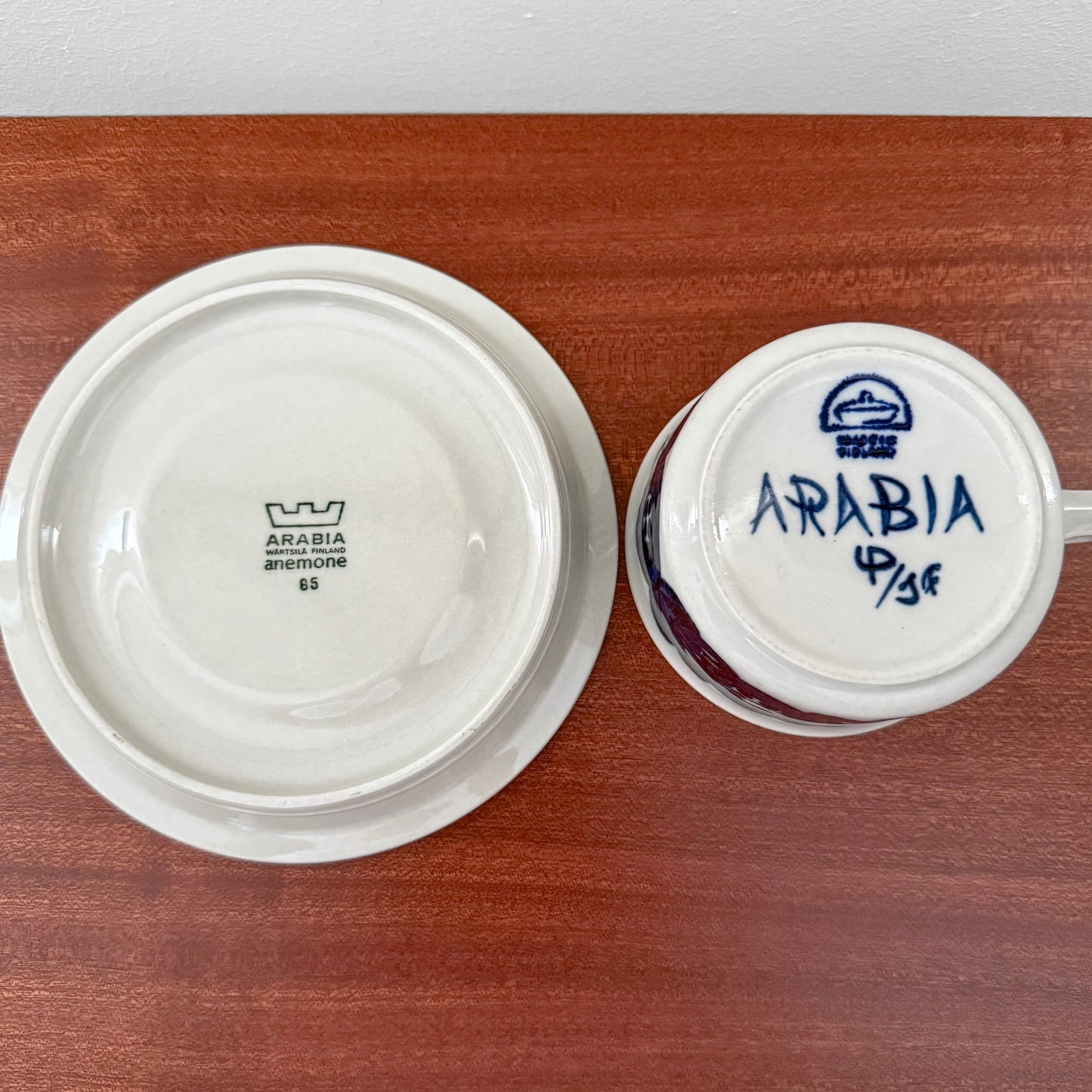 Bottom view of Arabia Finland Anemone Tea Cup with Saucer showing vintage maker’s marks on white ceramic against a wooden surface.