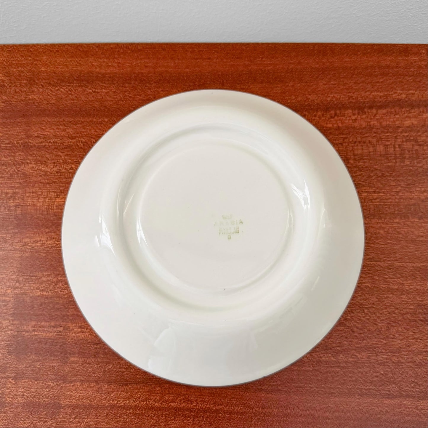 Back view of the Arabia Finland Emilia Large Cocoa Cup with Saucer showing the vintage maker's mark on the white ceramic saucer placed on a wooden surface.