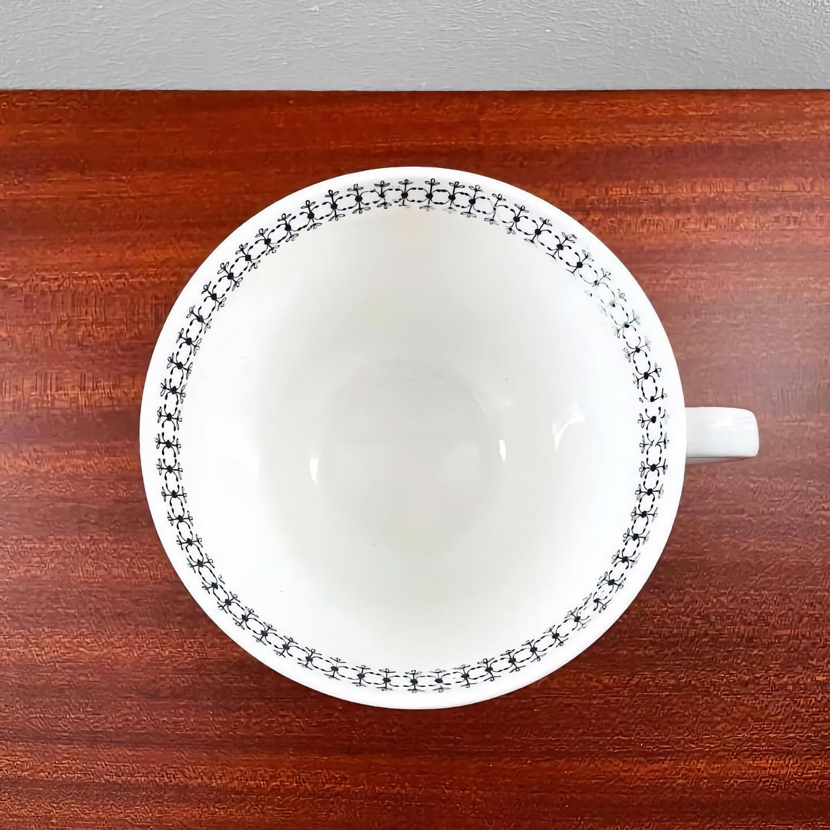 Arabia Finland Emilia Large Cup with TV Plate showing the white ceramic cup top view with delicate black decorative pattern around the rim, set on a wooden surface.