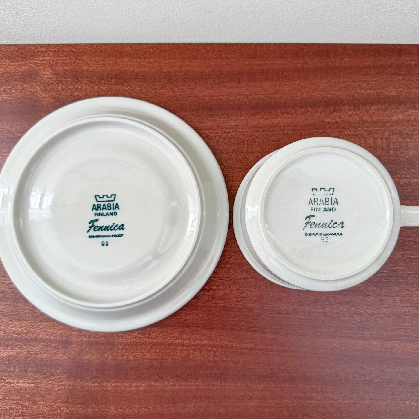 Bottom view of Arabia Finland Fennica Tea Cup with Saucer displaying vintage ceramic maker's marks and logos on a wooden surface, highlighting authentic Scandinavian craftsmanship.
