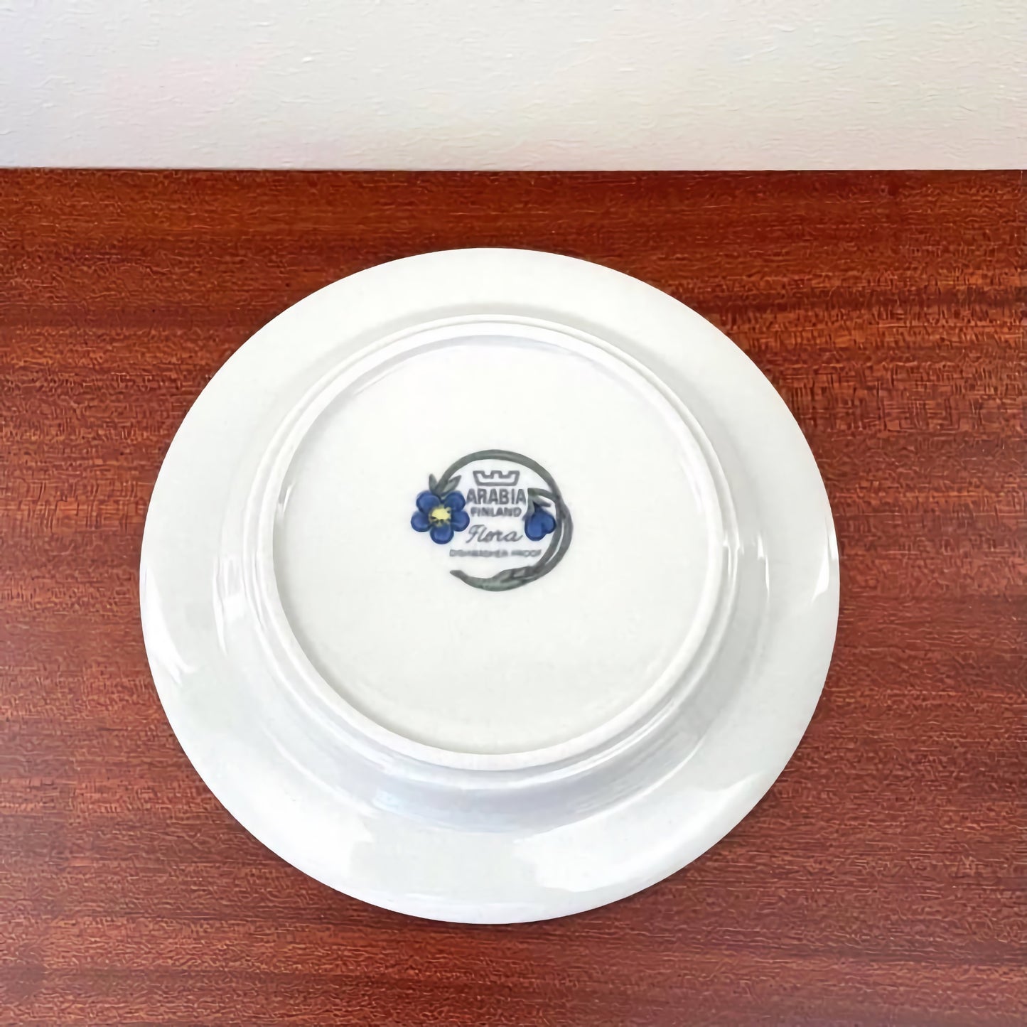 Back view of the Arabia Finland Flora Coffee Cup Trio Set cake plate showing the logo and floral design on white ceramic surface on a wooden table.