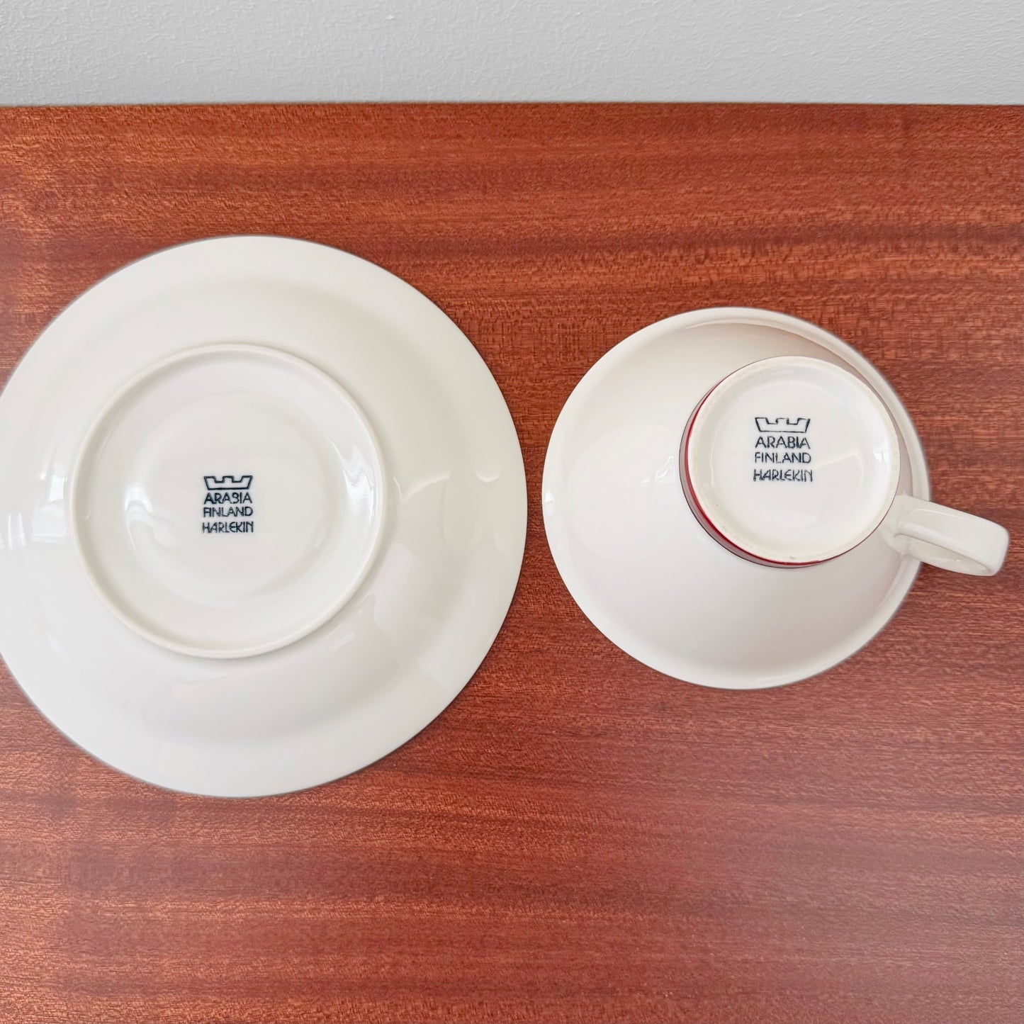 Arabia Finland Harlekin Red Hat Tea Cup with Saucer showing the underside stamps of authentic vintage ceramic drinkware on a wooden surface.