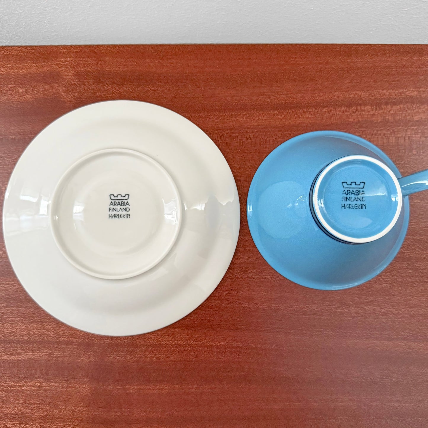 Arabia Finland Harlekin Turquoise Tea Cup with Saucer showing the underside stamps, highlighting authentic vintage Nordic ceramic craftsmanship on a wooden surface.