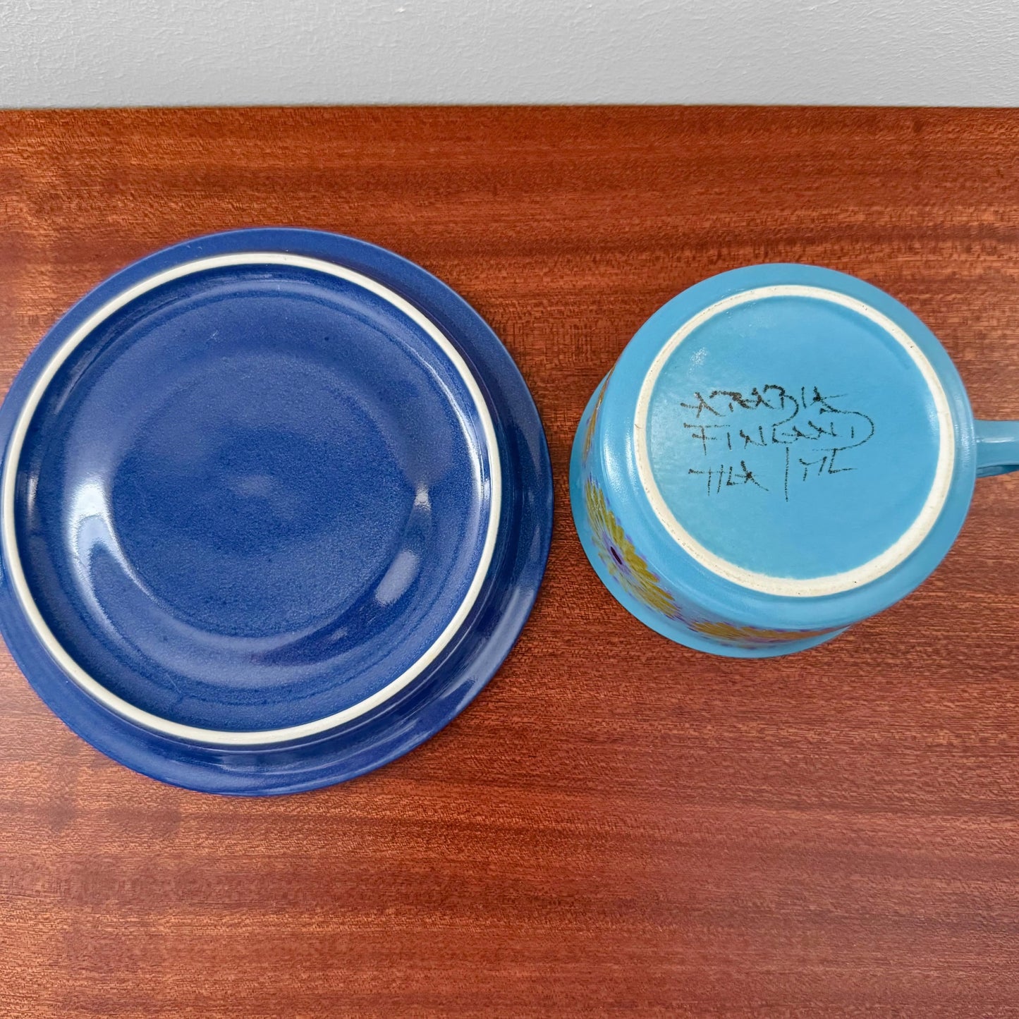 Arabia Finland Hilkka-Liisa Ahola Blue Tea Cup with Saucer shown from above on a wooden surface, featuring hand-painted markings and vibrant blue hues.