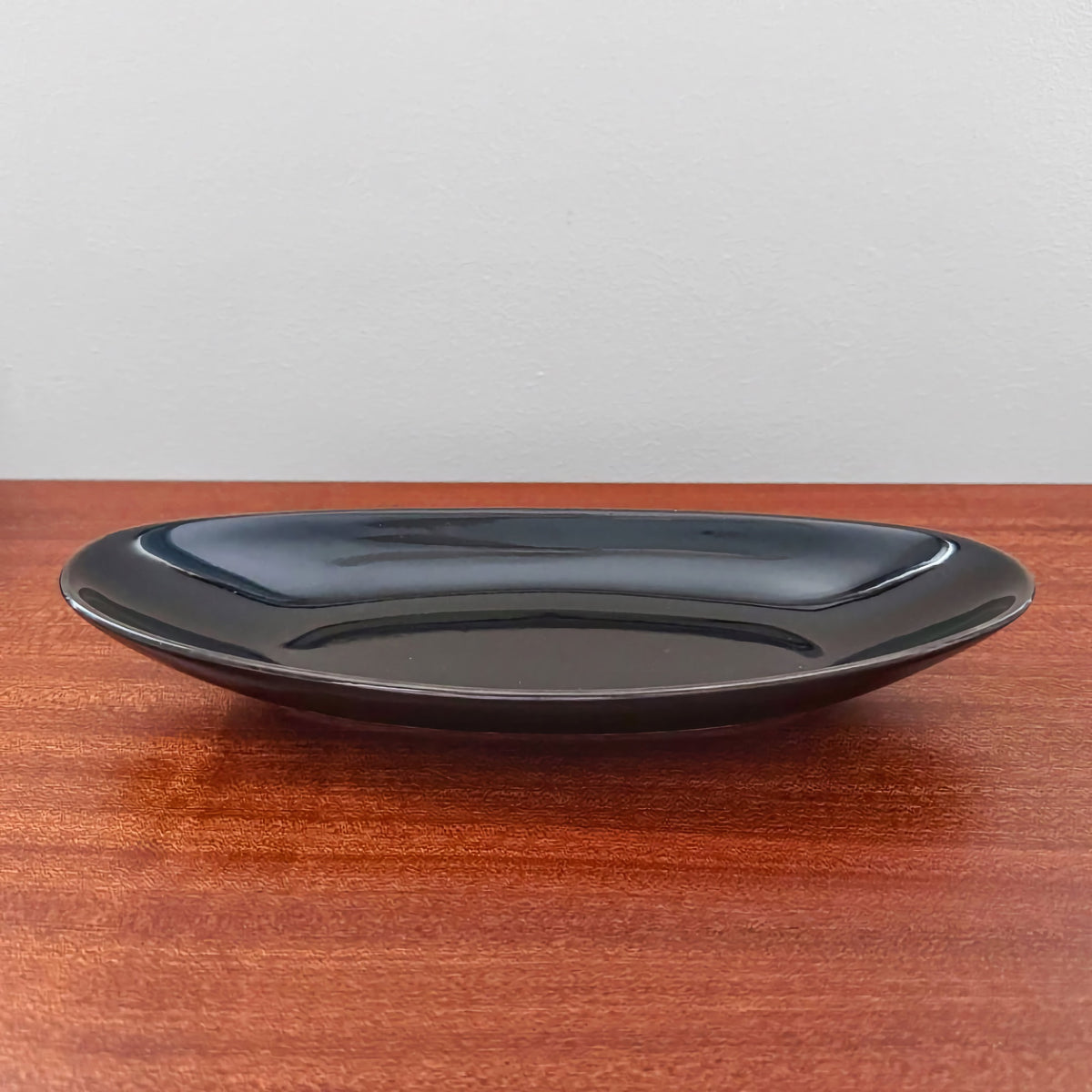 Arabia Finland Kilta Black Herring Plate displayed on a wooden surface, showcasing its sleek black ceramic design by Kaj Franck from the 1950s with a vintage finish.