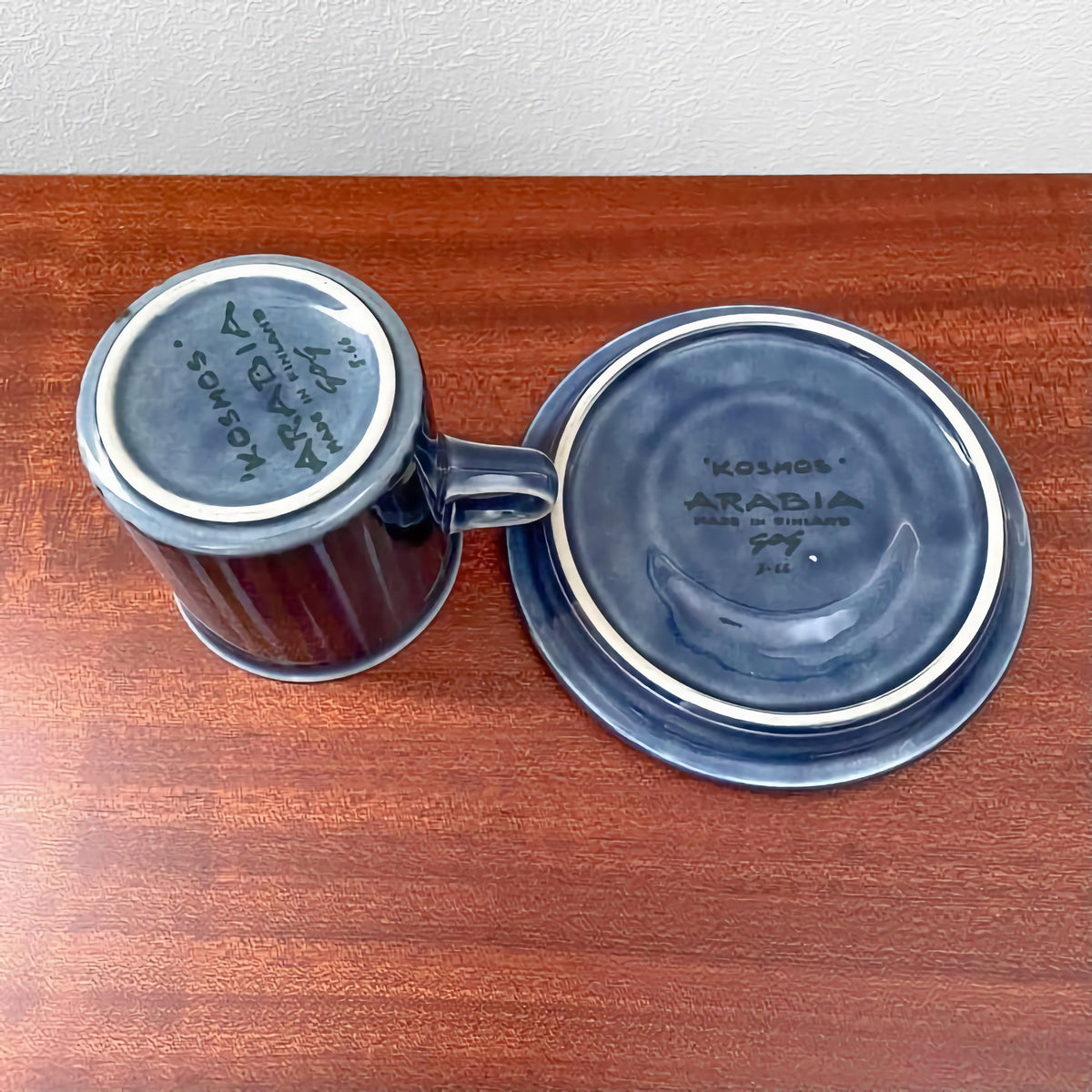 Two pieces from the Arabia Finland Kosmos Blue Coffee Cup Trio Set including a blue ceramic cup and matching saucer with signature markings visible on the bases.