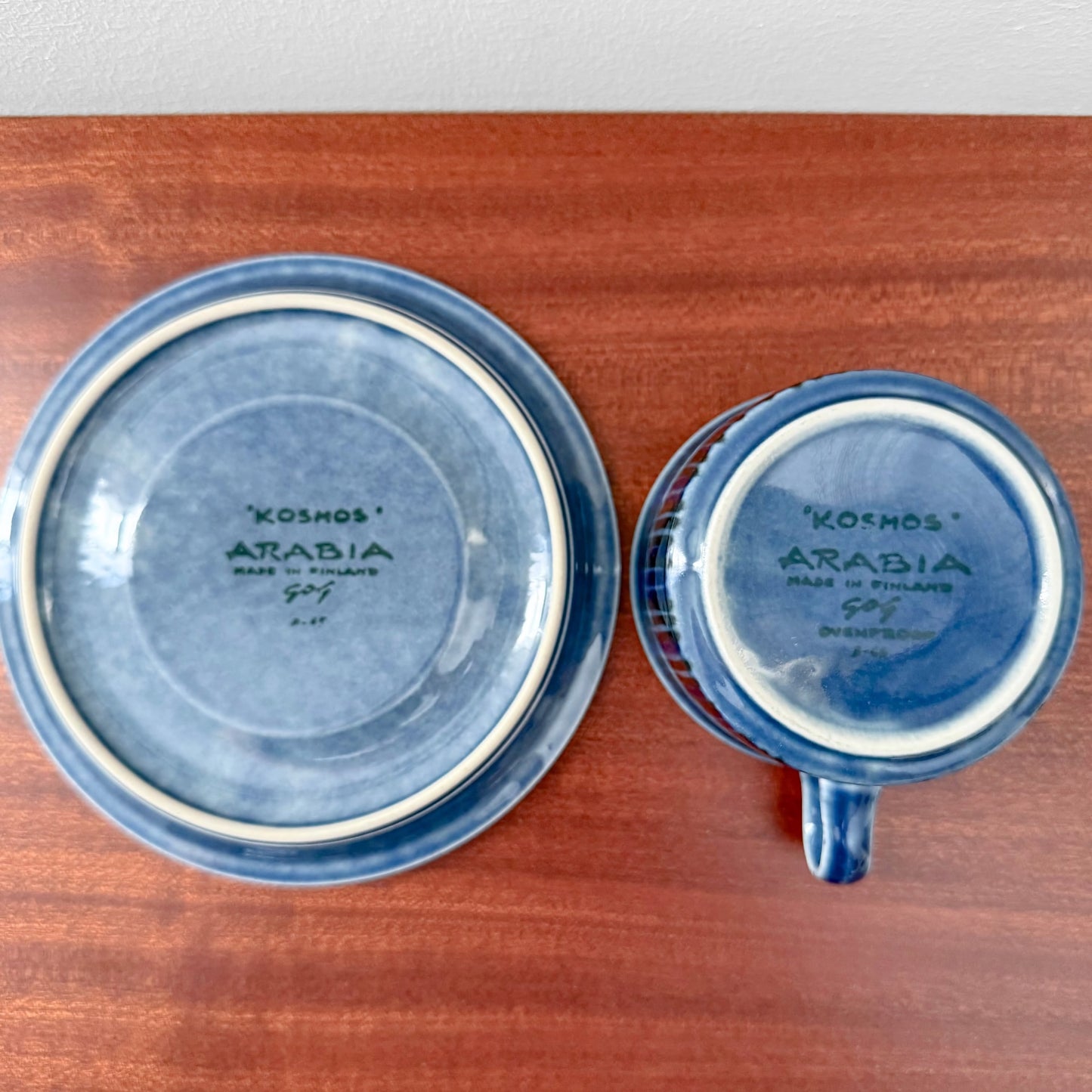 Bottom view of a vintage Arabia Finland Kosmos Blue Tea Cup with Saucer placed on a wooden surface, showing the manufacturer's markings and signature design.