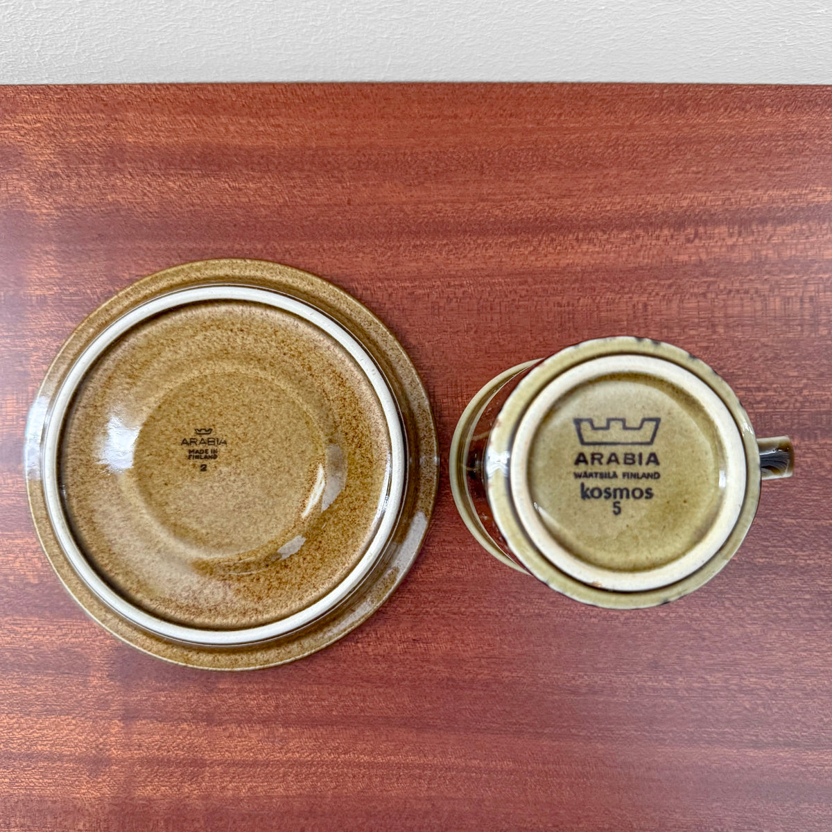 Arabia Finland Kosmos Coffee Cup with Saucer shown from the bottom view, featuring vintage ceramic drinkware with stamped maker’s marks on a wooden surface.