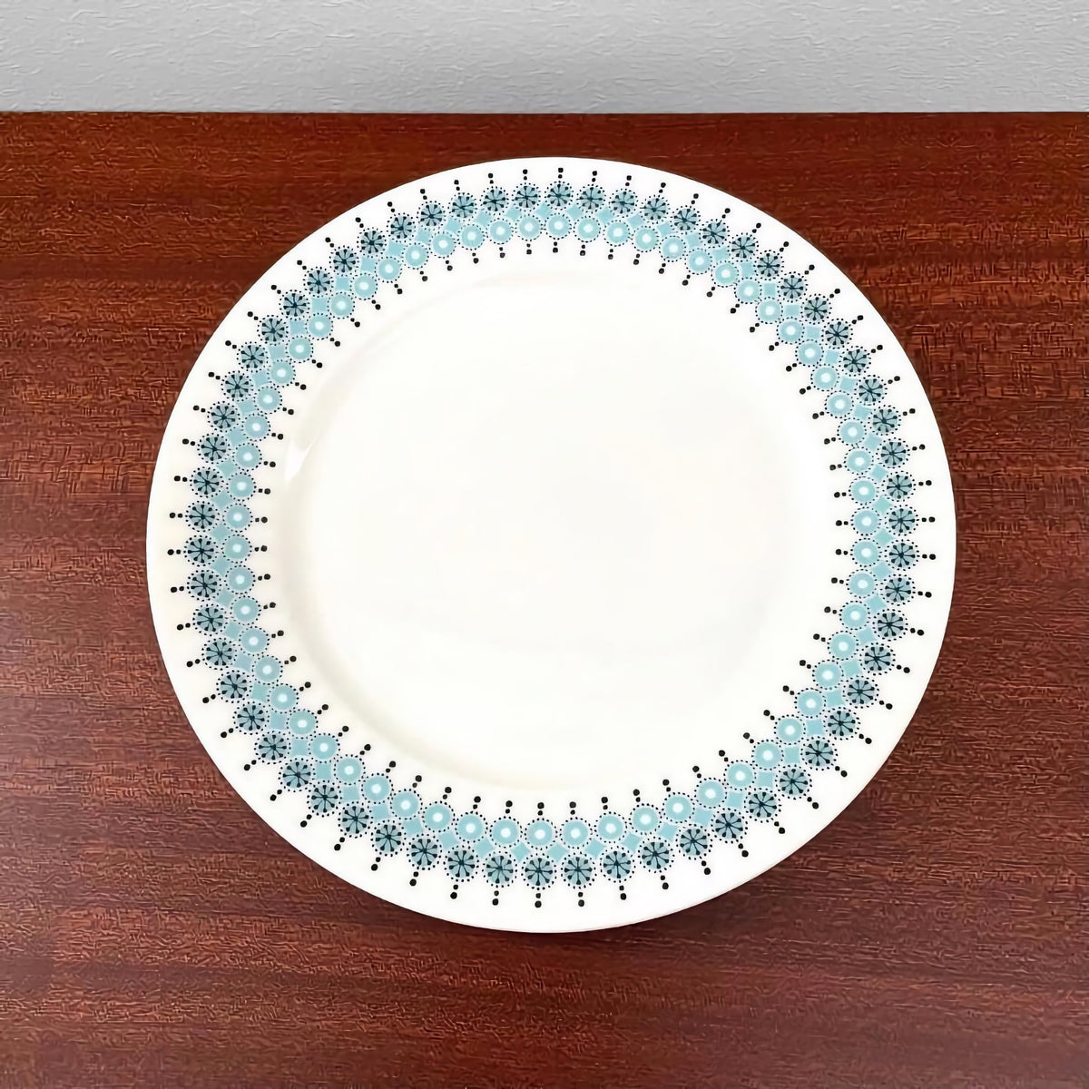 Cake plate from the Arabia Finland Louhi Coffee Cup Trio Set featuring a vintage 1970s Nordic design with blue and black floral patterns on white ceramic, displayed on a wooden surface.