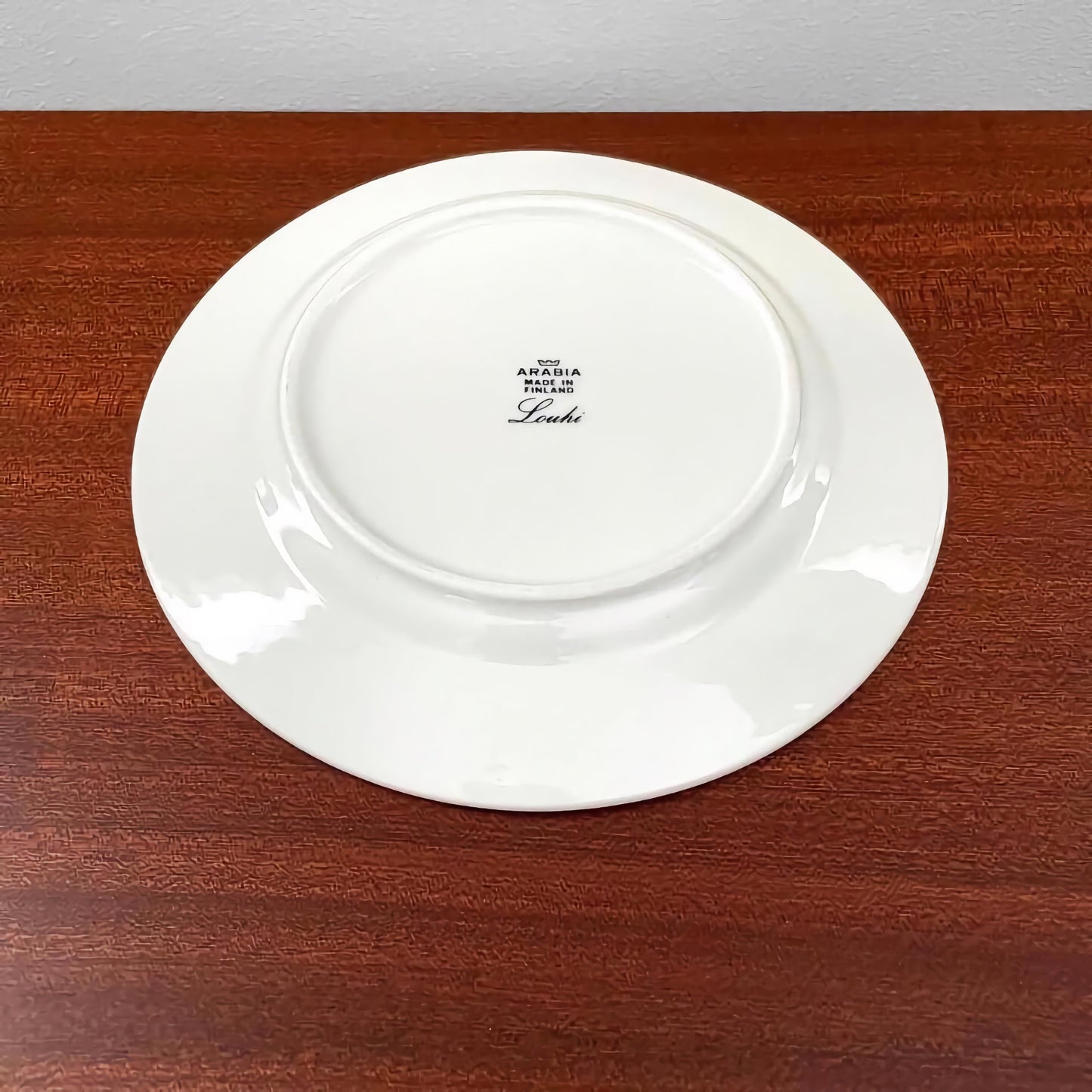 White ceramic cake plate shown from the underside with Arabia Finland Louhi Coffee Cup Trio Set maker's mark on a wooden surface.