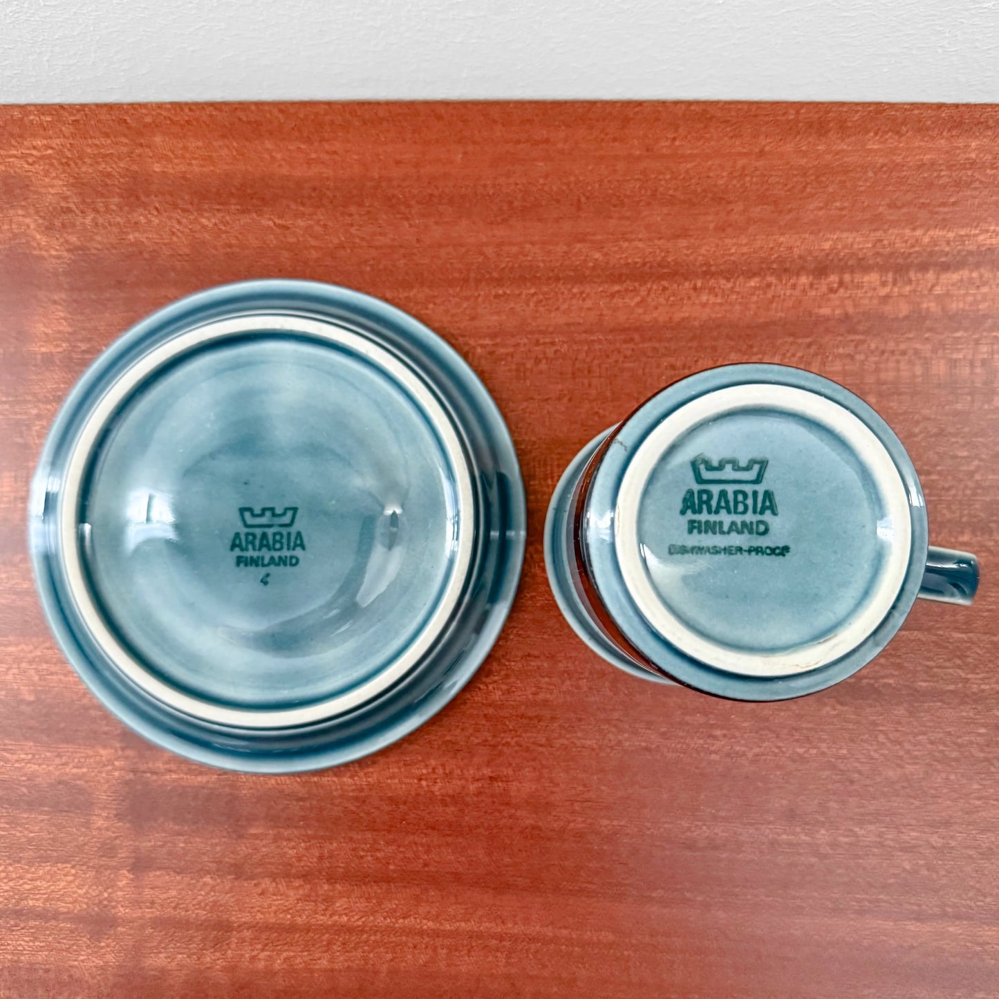 Arabia Finland Meri Coffee Cup with Saucer showing the bottom stamps highlighting vintage Nordic ceramic craftsmanship in blue glaze on wooden surface.