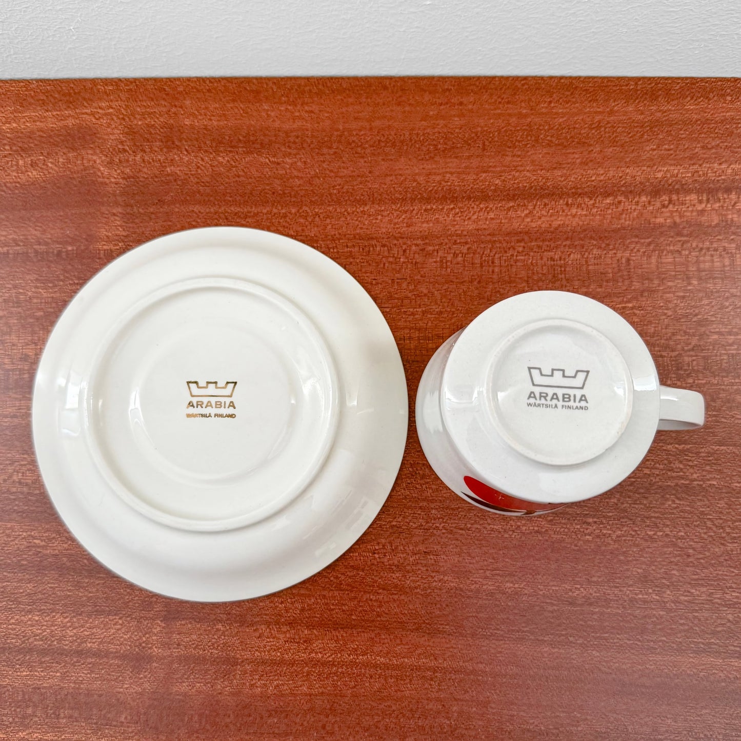 Bottom view of a vintage Arabia Finland Omena Coffee Cup with Saucer showing the maker’s mark on white ceramic placed on a wooden surface in Nordic Wares Store.