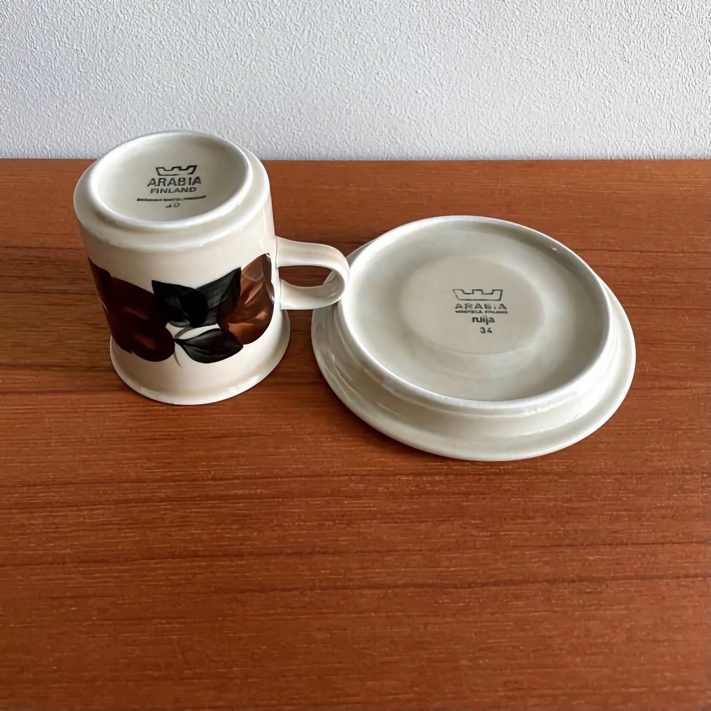 Arabia Finland Ruija Coffee Cup with Saucer showing vintage ceramic cup with brown and black leaf design alongside matching saucer on wooden surface.