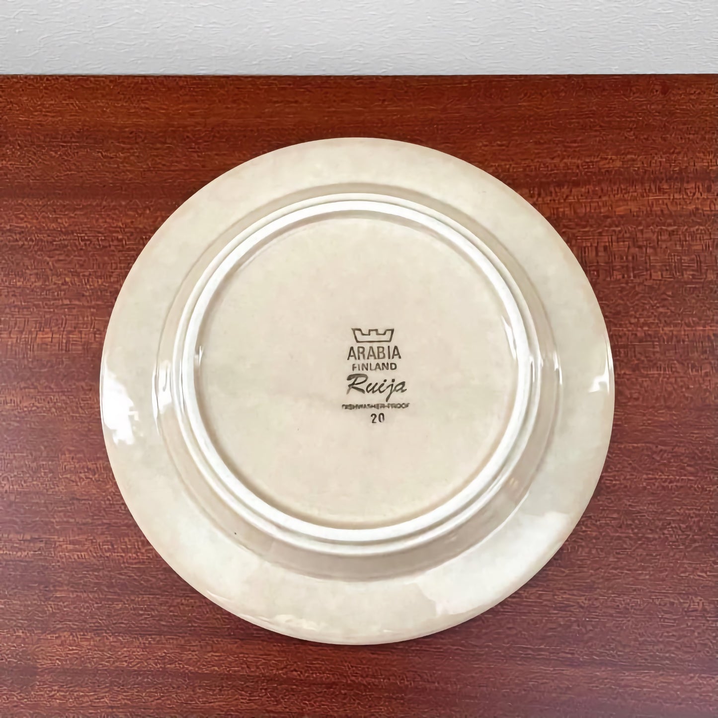 Backside of a vintage ceramic plate from the Arabia Finland Ruija Coffee Cup Trio Set, showing the maker’s mark and signature on a white-glazed surface.