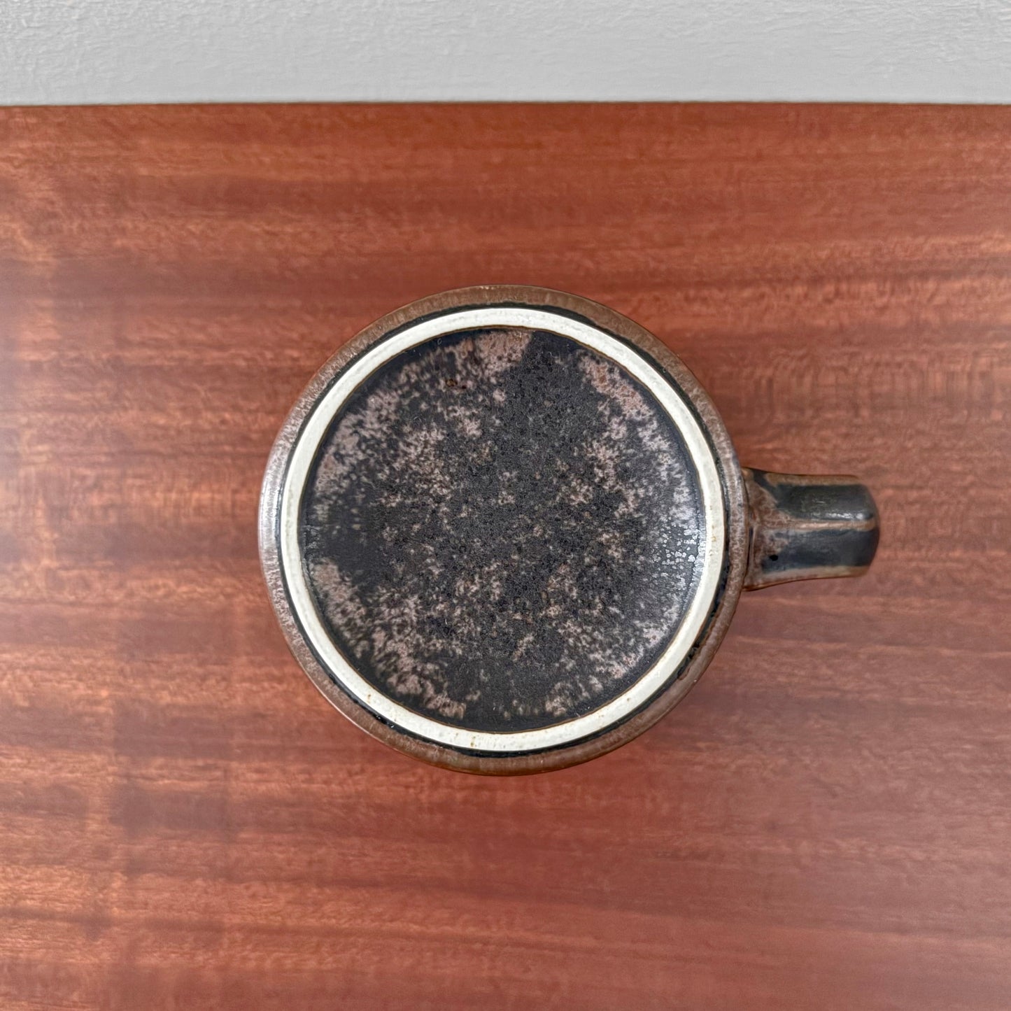 Top view of a vintage Arabia Finland Ruska Large Mug showing its speckled brown ceramic base and handle, placed on a wooden surface.