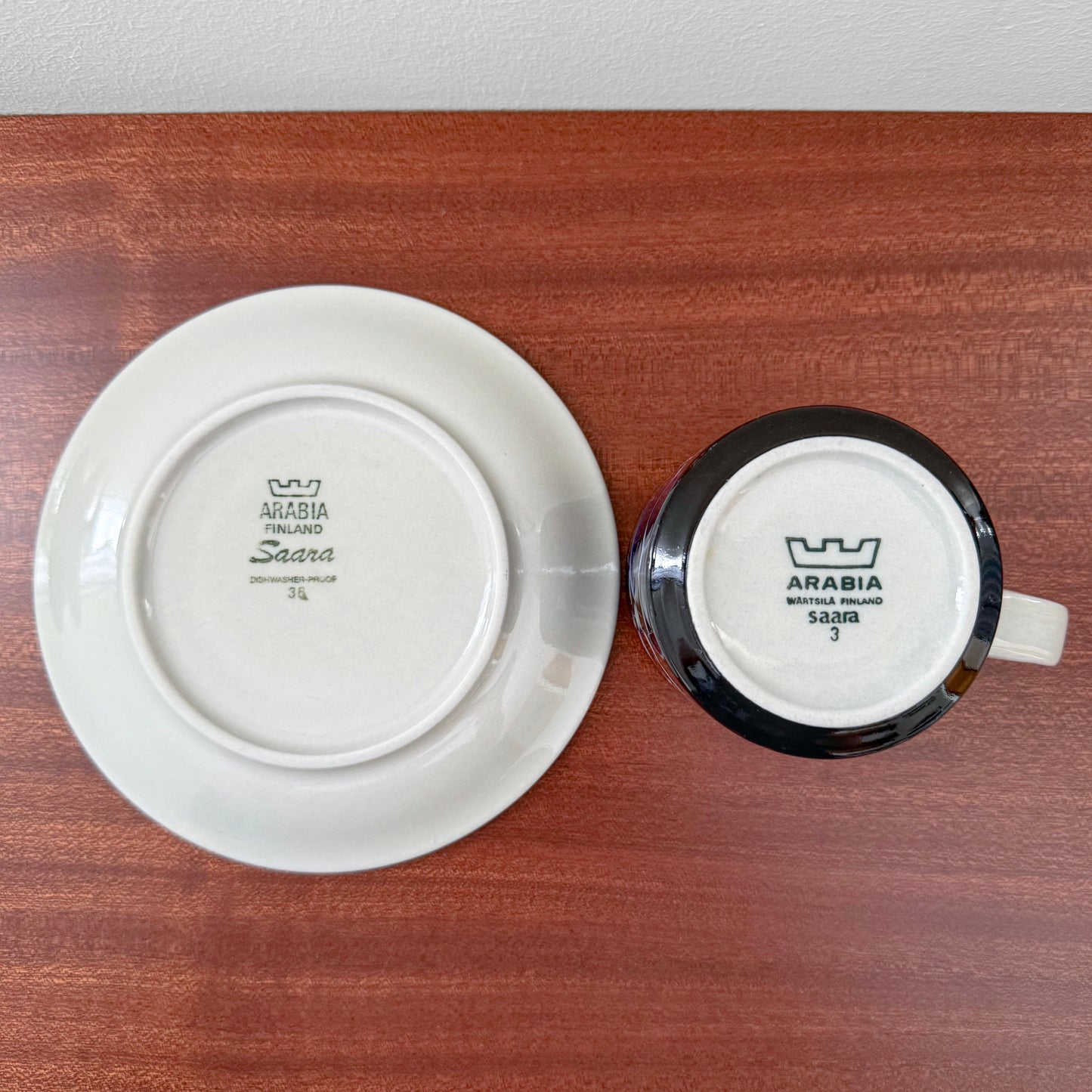 Arabia Finland Saara Tea Cup with Saucer showing the bottom stamps on the white ceramic base placed on a wooden surface, highlighting vintage Nordic ceramics craftsmanship.