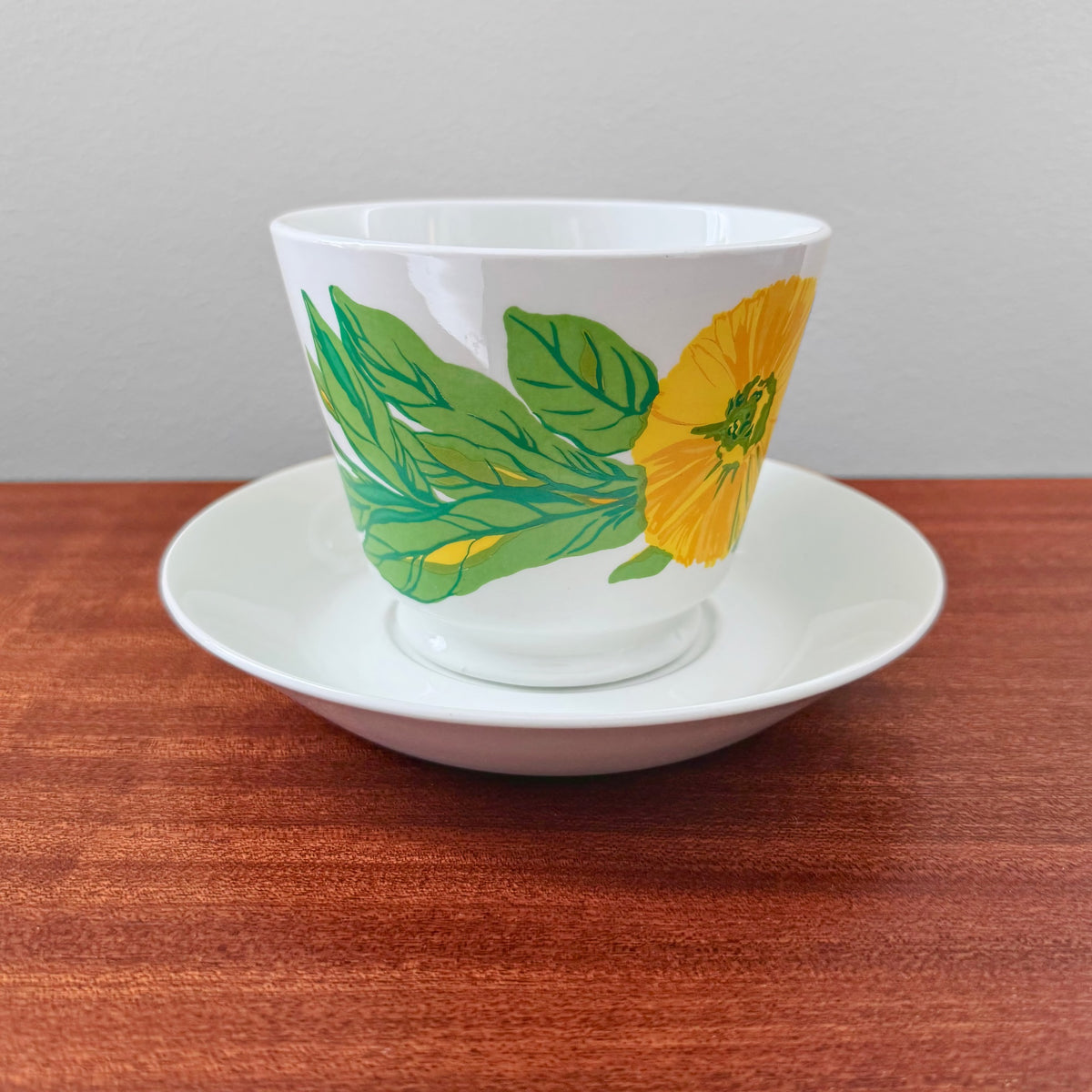 Arabia Finland Suvi Large Cocoa Cup with Saucer featuring a 1970s vintage design by Gunvor Olin-Grönqvist with vibrant green leaves and a yellow flower on white ceramic.