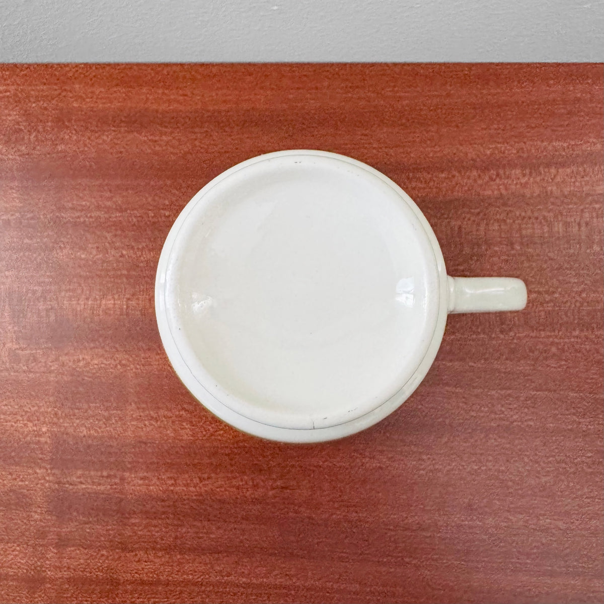 Arabia Finland Suvi Large Cocoa Cup with Saucer showing a top view of a white ceramic cup with handle on a wooden surface, highlighting its vintage Nordic design and craftsmanship.