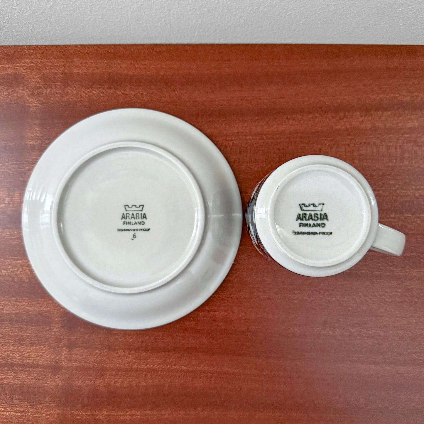 Arabia Finland Taika Coffee Cup with Saucer shown from the bottom, featuring vintage ceramic markings on white glazed ceramic against a wooden surface.