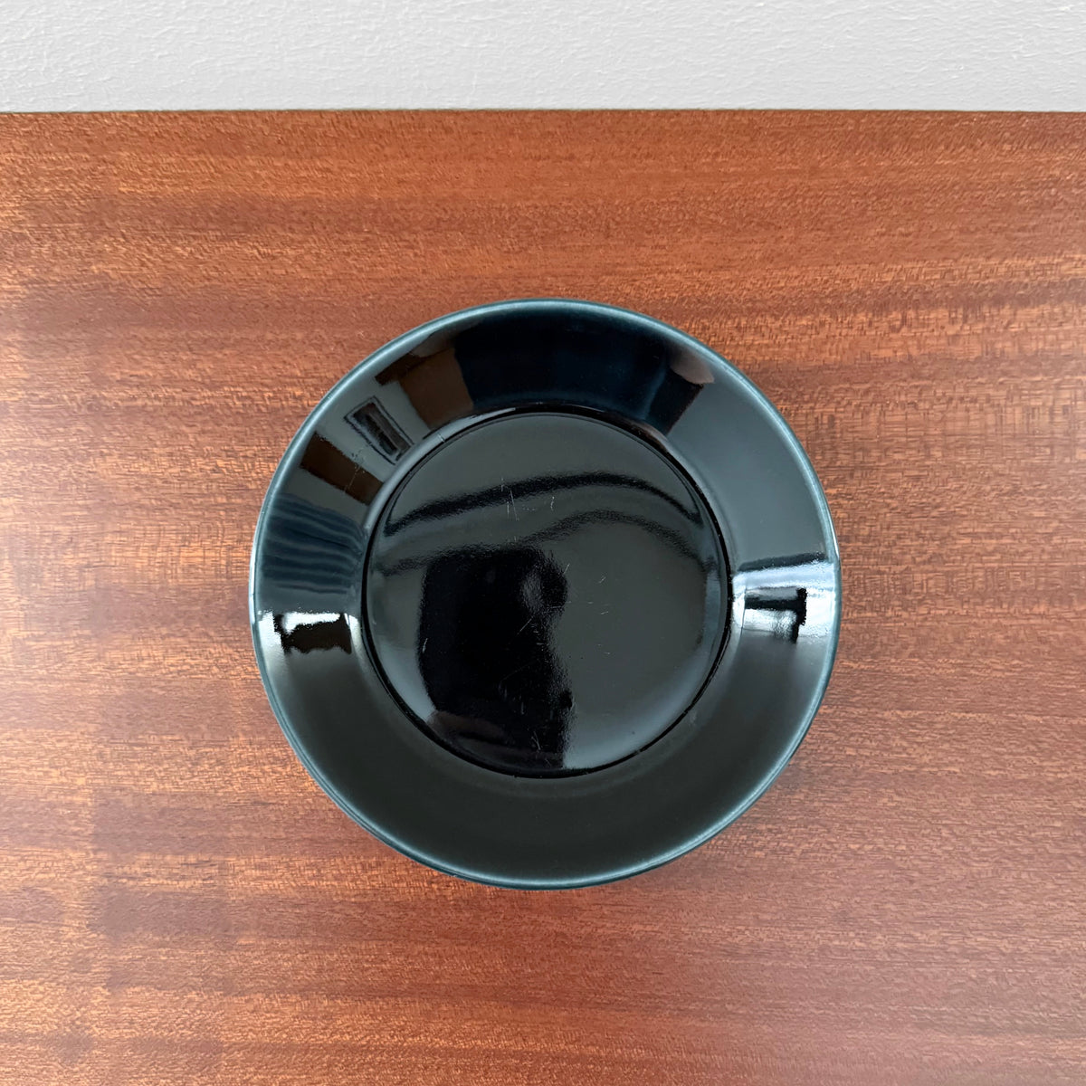 Arabia Finland Teema Black Coffee Cup with Saucer shown from above on a wooden surface, highlighting its glossy black ceramic finish and clean Scandinavian design.