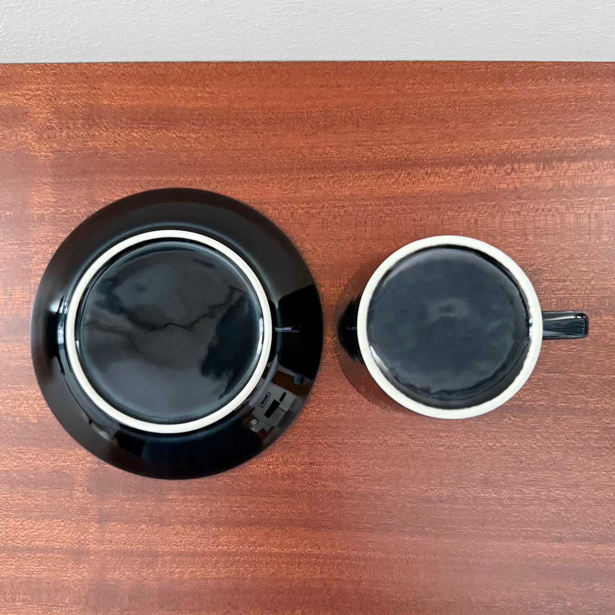 Top view of Arabia Finland Teema Black Coffee Cup with Saucer showcasing glossy black ceramic drinkware with white rim details on a wooden surface.