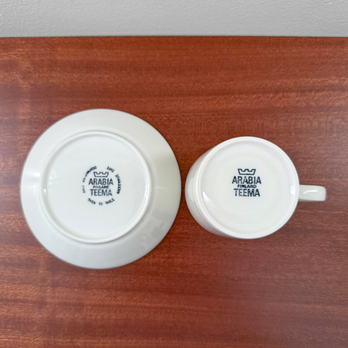 Bottom view of Arabia Finland Teema White Coffee Cup with Saucer showing authentic maker’s marks stamped on white ceramic surface on a wooden table.