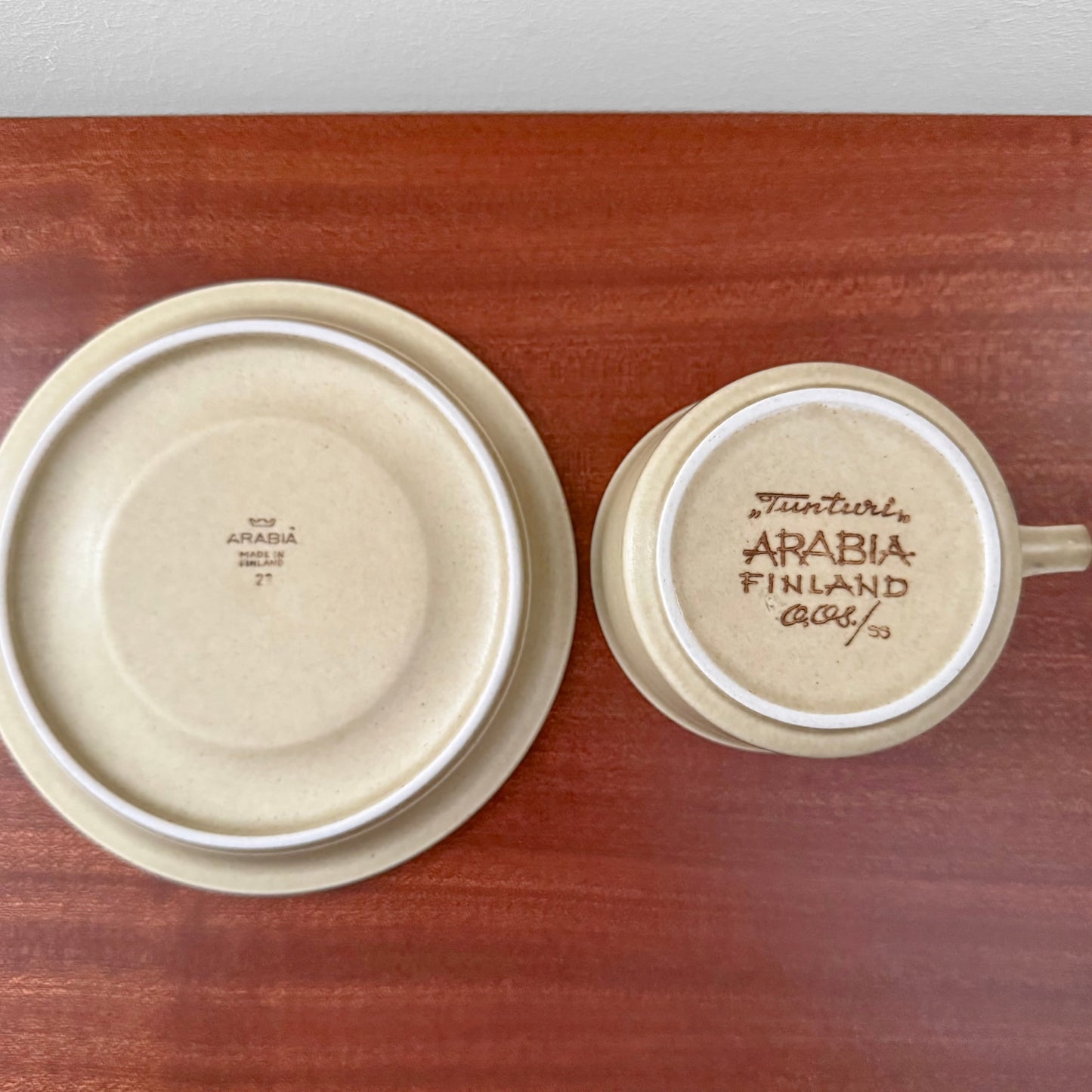 Bottom view of Arabia Finland Tunturi Tea Cup with Saucer showing vintage markings on ceramic in beige tone on a wooden surface.