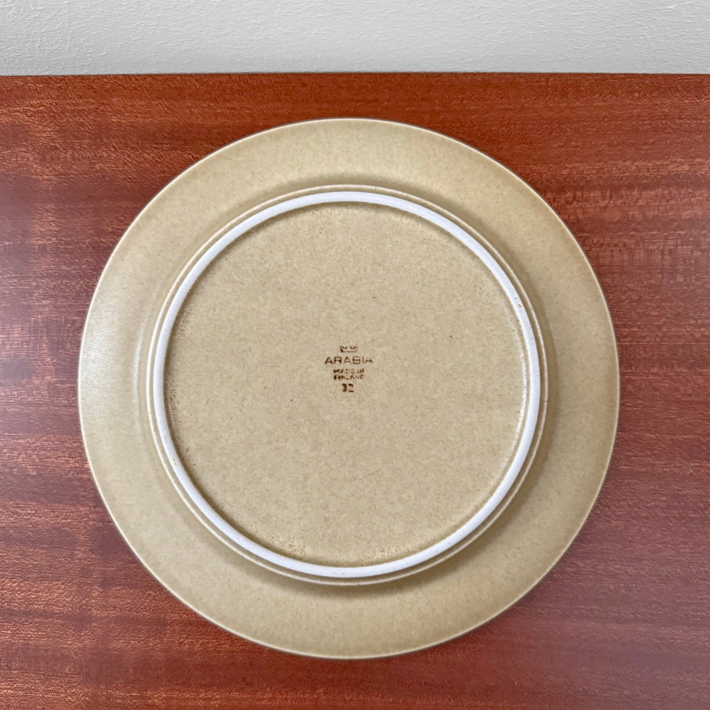 Bottom view of a beige ceramic plate from the Arabia Finland Tunturi Tea Cup Trio Set, showcasing the maker's mark on a wooden surface.