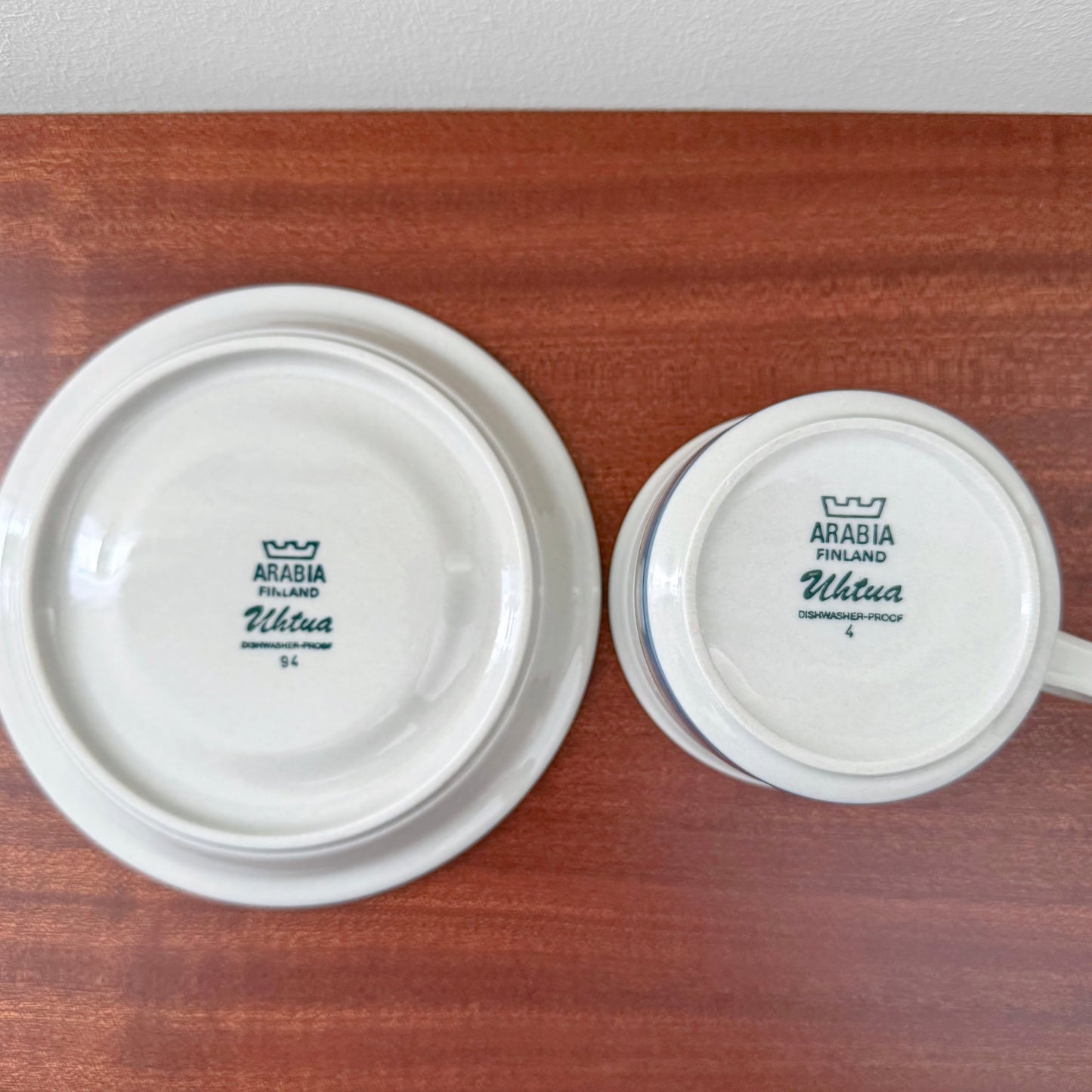 Bottom view of Arabia Finland Uhtua Tea Cup with Saucer showing vintage maker’s marks on white ceramic against a wooden surface in Nordic Wares Store setting.