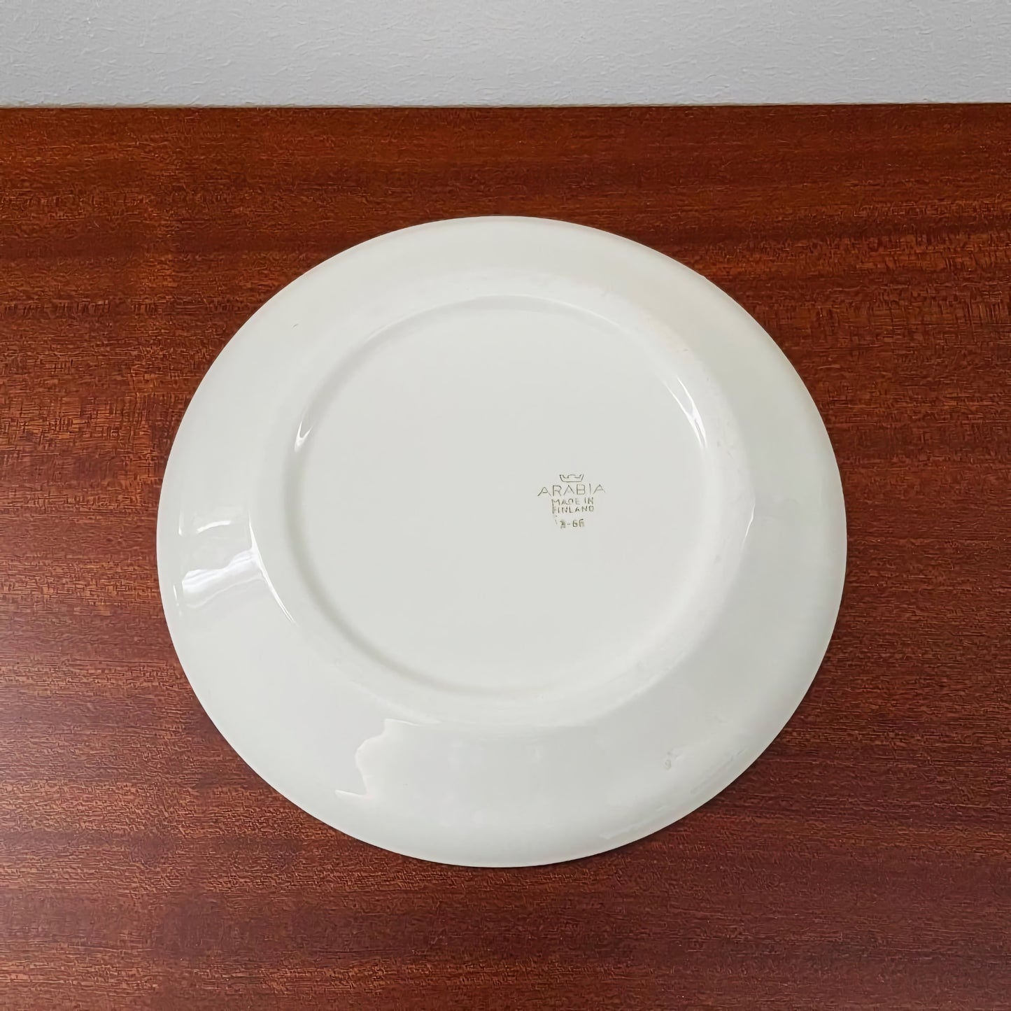 Back view of a white ceramic plate from the Arabia Finland Valmu Tea Cup Trio Set, showing vintage markings on its base, placed on a wooden surface.
