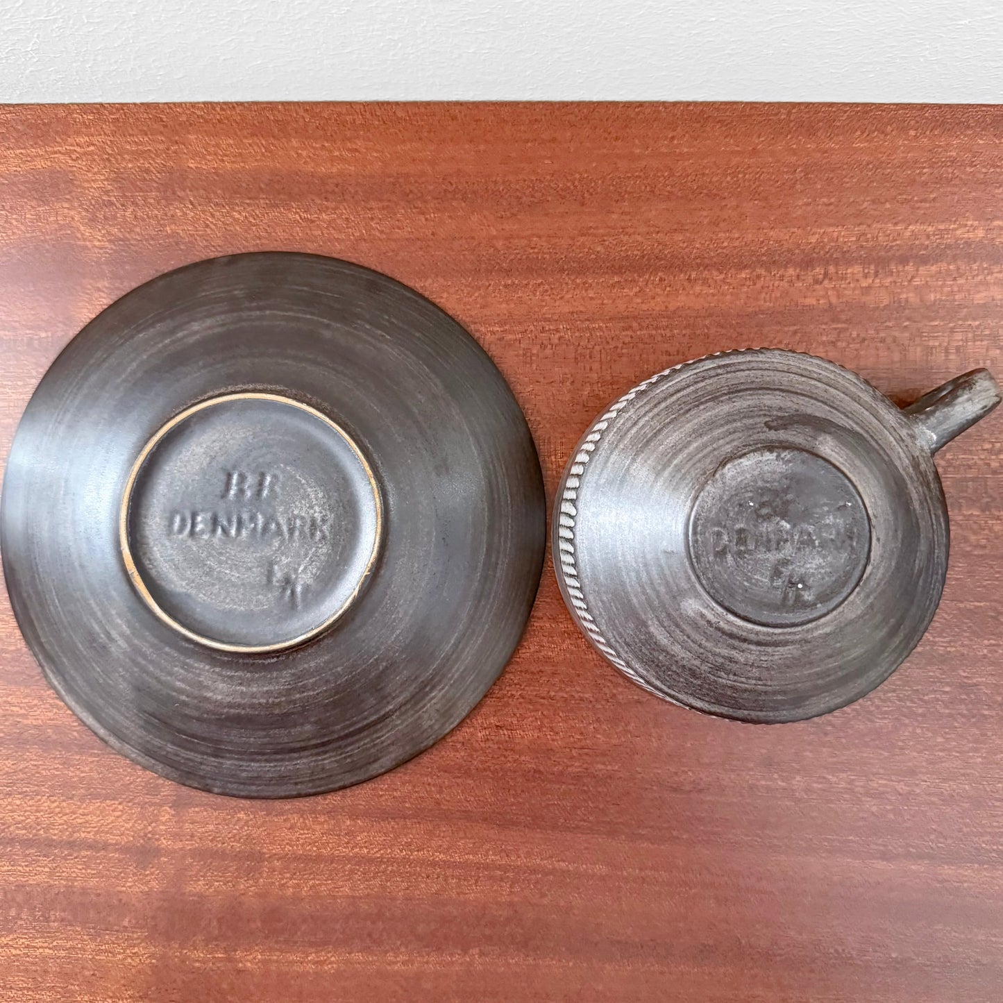 BR Keramik Amazonas Tea Cup with Saucer viewed from below, showing textured dark ceramic craftsmanship and embossed maker marks on a wooden surface.