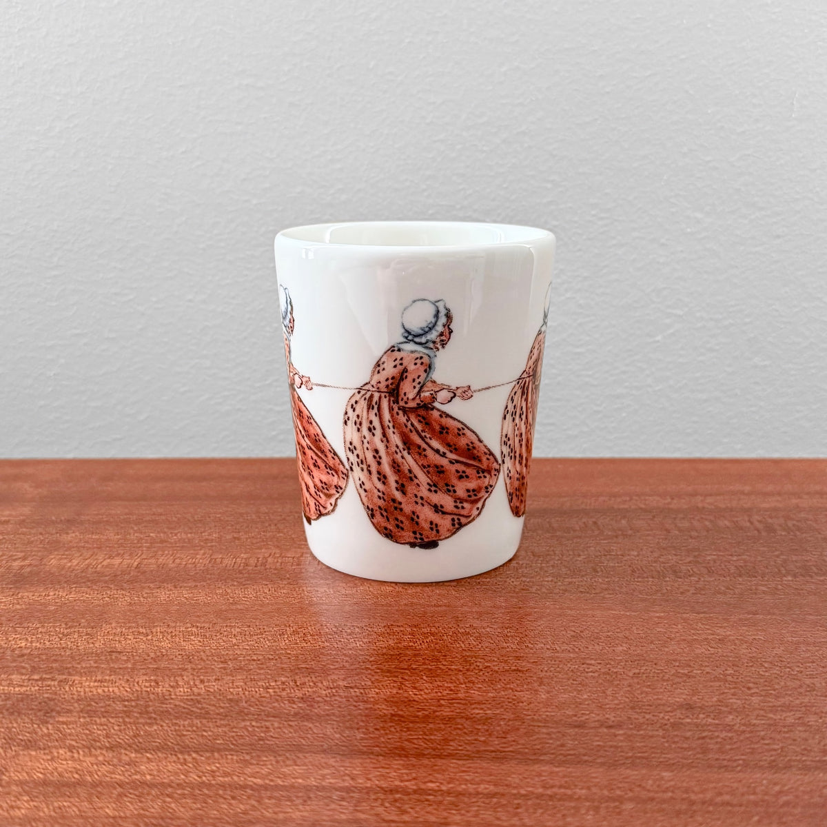 White ceramic mug featuring vintage-style illustrations of a girl in a patterned dress pulling a rope, Elsa Beskow Aunt Brown Mug from Nordic Wares Store.