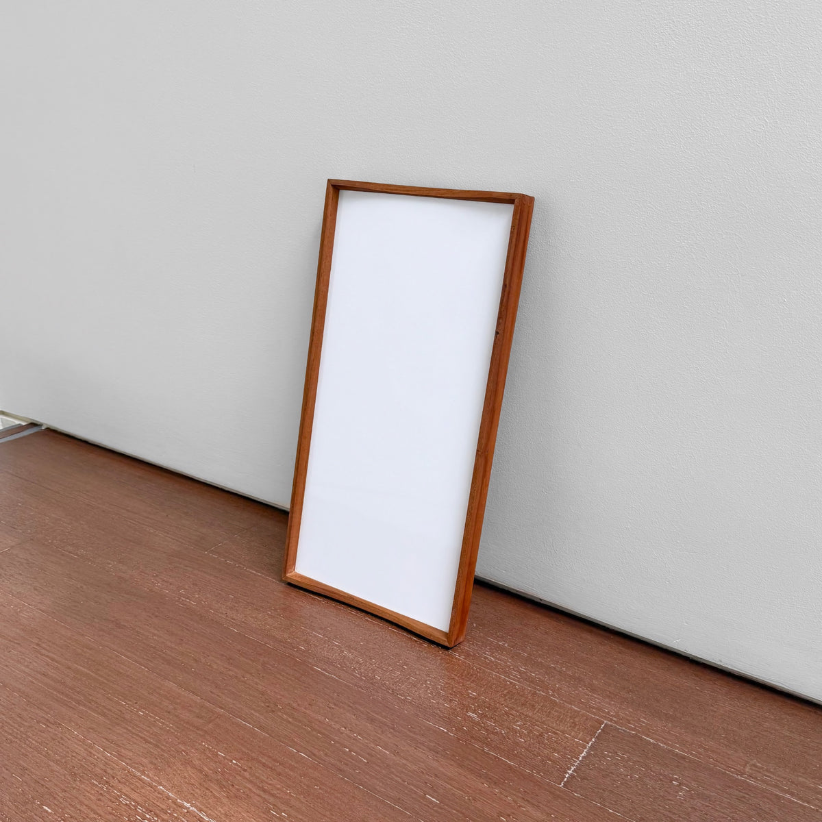 Finn Juhl Architectmade Turning Tray (Small, Black-White) standing upright against a gray wall on a wooden floor, featuring a rectangular wood frame with a clean black and white laminate surface.