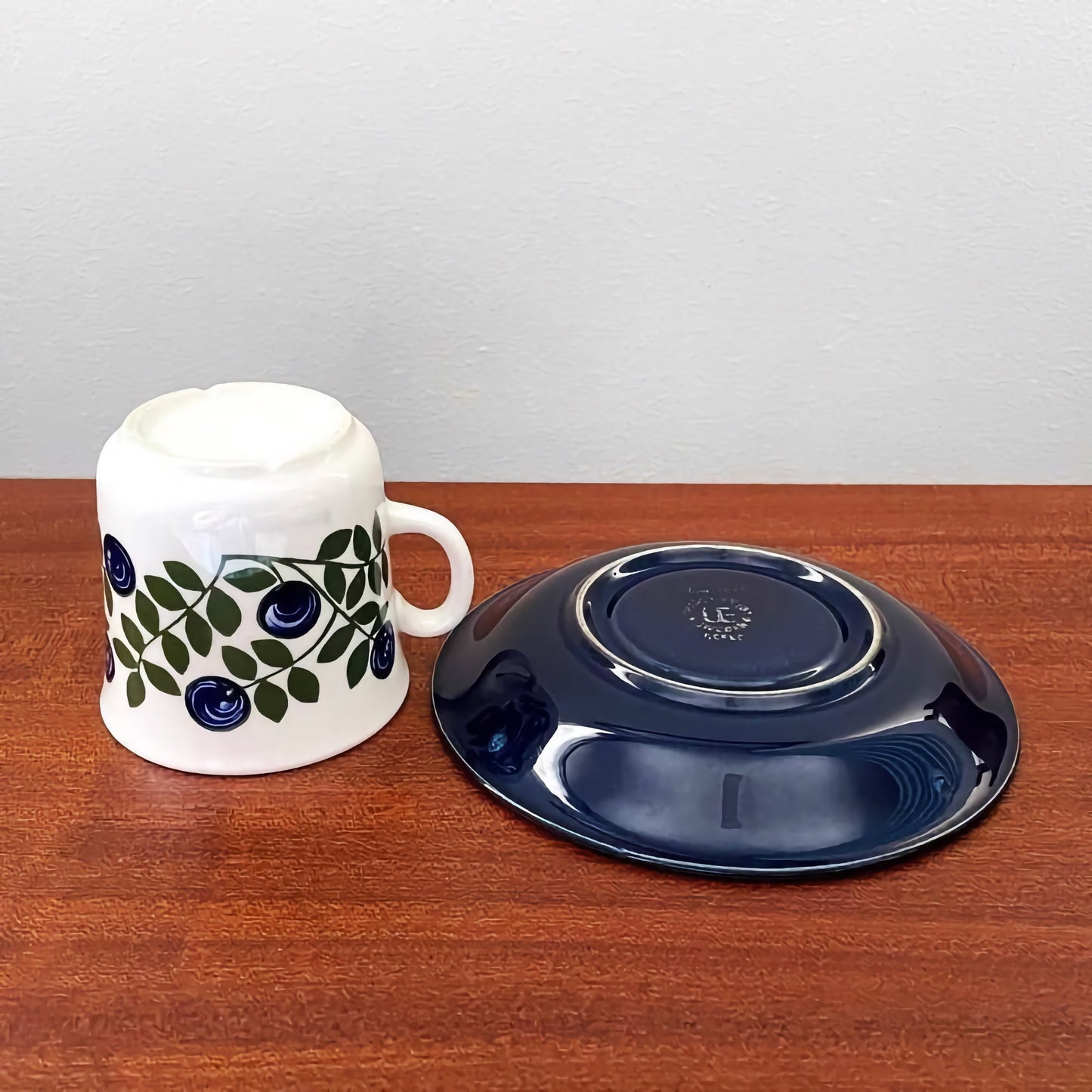 Upsala-Ekeby/Gefle Blåbär Coffee Cup with Saucer featuring a white ceramic cup decorated with blue berry and green leaf patterns alongside a deep blue saucer, showcasing vintage Scandinavian design.