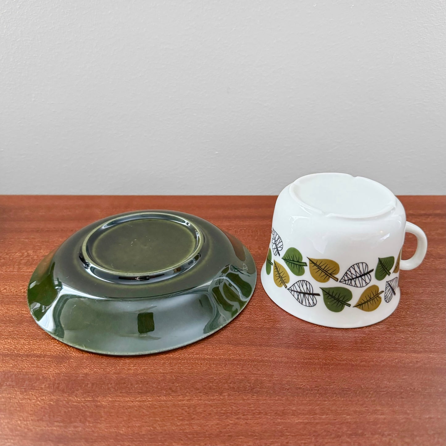 Upsala-Ekeby/Gefle Bladranka Tea Cup with Saucer featuring a white cup decorated with green and brown leaf patterns and a matching dark green saucer, vintage Scandinavian drinkware.