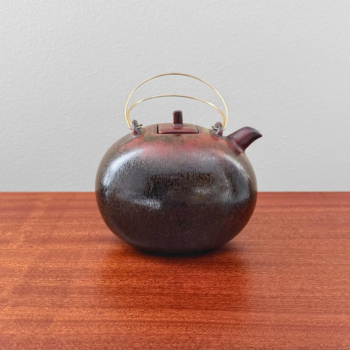 Gösta Grähs Rörstrand Brown Stoneware Teapot with rounded body, dark brown textured ceramic surface, and thin curved metal handle, showcasing vintage Nordic craftsmanship.