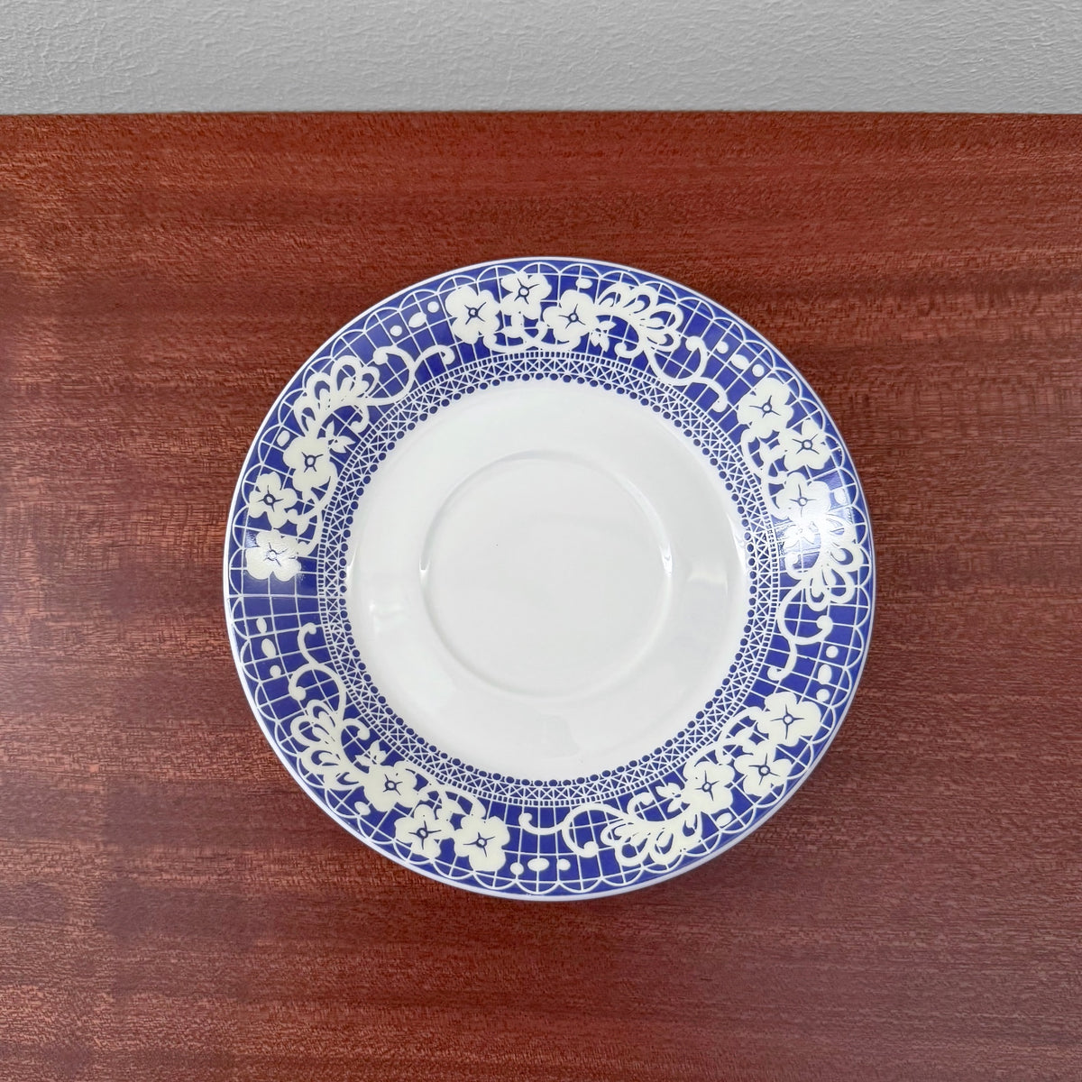 Gustavsberg Ada Coffee Cup with Saucer featuring a vintage blue and white floral patterned ceramic saucer on a wooden surface, showcasing Scandinavian design craftsmanship.