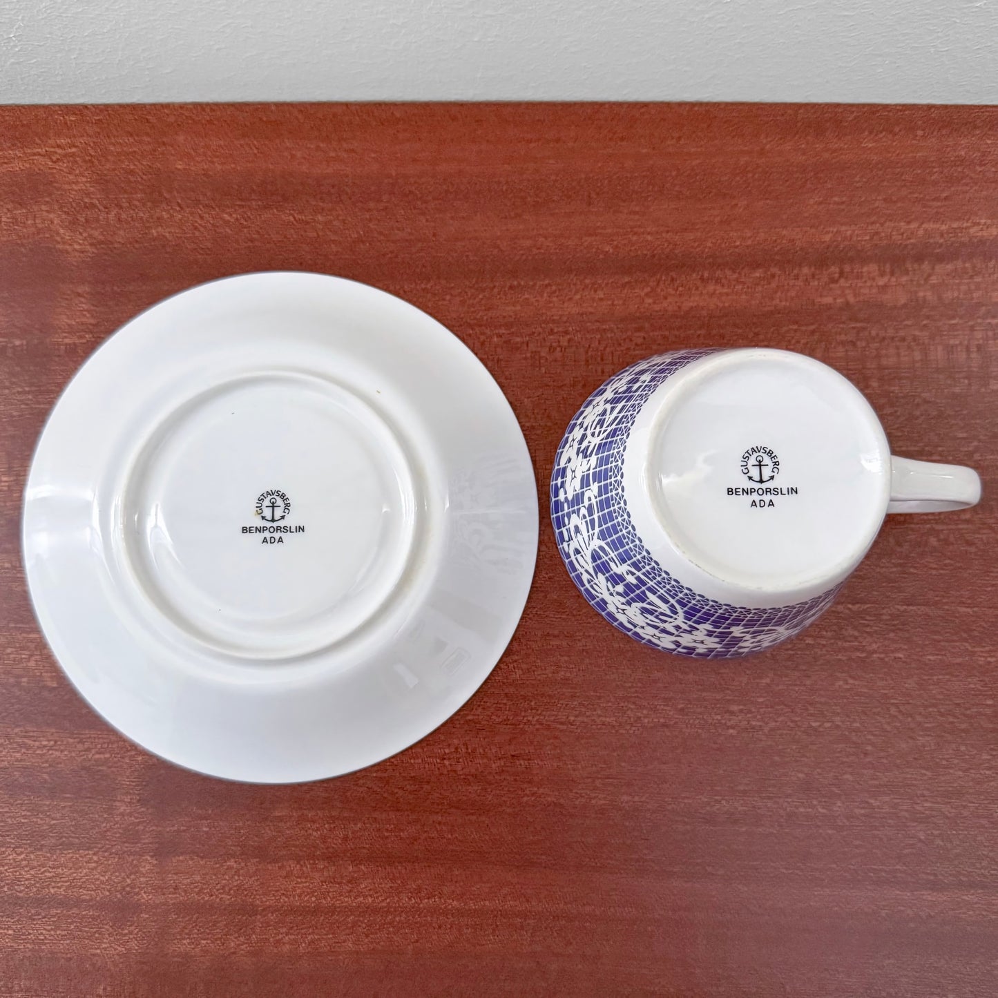 Bottom view of vintage Gustavsberg Ada Coffee Cup with Saucer showing the maker's mark by Stig Lindberg, featuring blue and white Scandinavian ceramic design on a wooden surface.