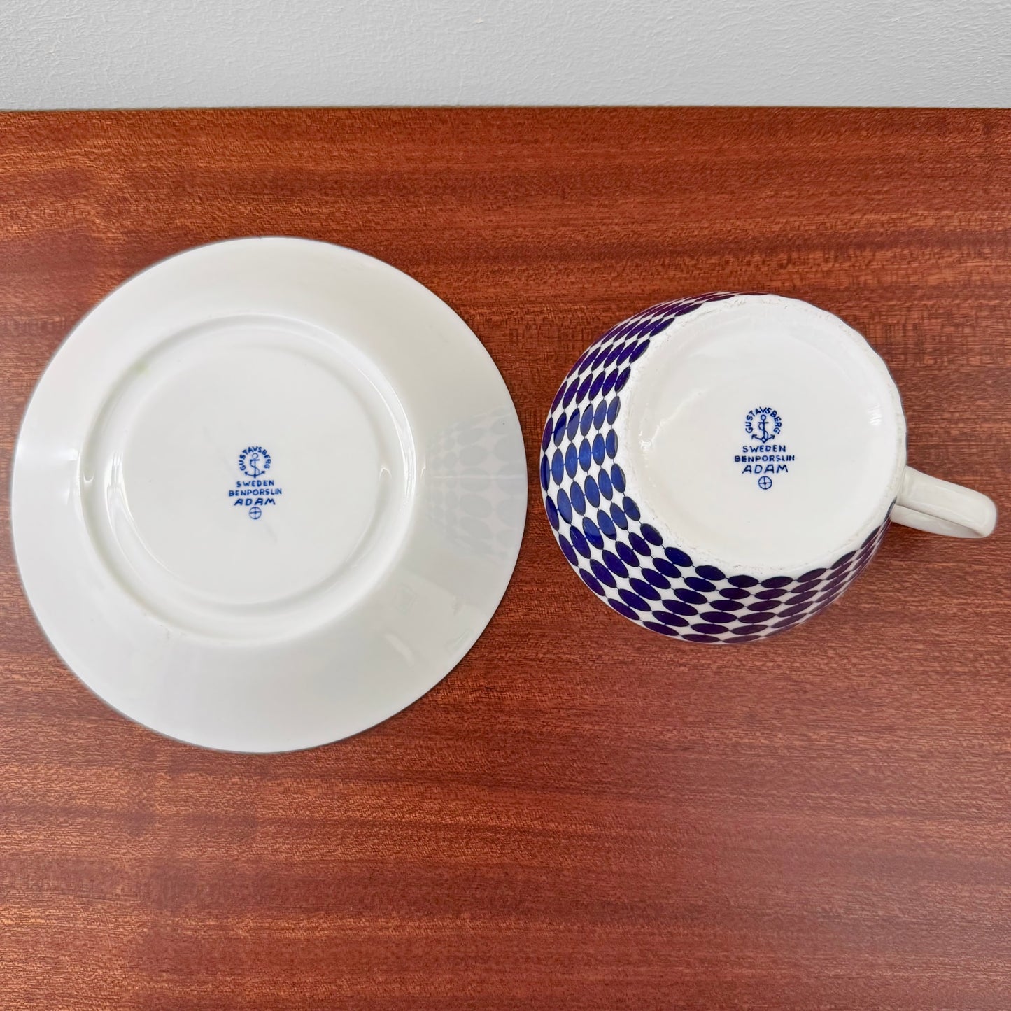 Gustavsberg Adam Tea Cup with Saucer showing the bottom stamps on white ceramic with a blue dot pattern on the cup, placed on a wooden surface.