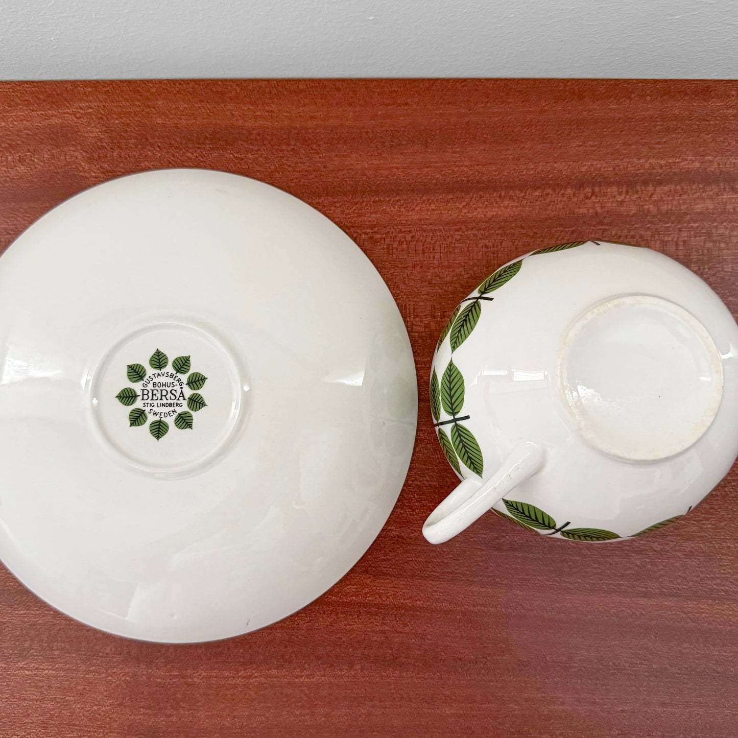 Vintage Gustavsberg Berså Large Breakfast Cup with Saucer showing green leaf pattern on ceramic with Stig Lindberg design from 1960s, displayed on wooden surface.
