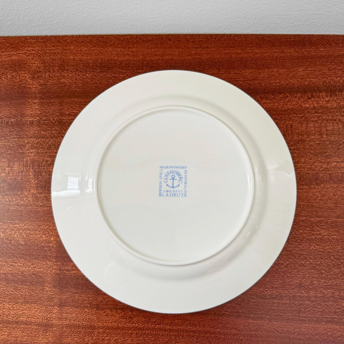 Back view of a vintage Gustavsberg Bladruta Coffee Cup Trio Set cake plate showing the blue maker’s mark on white ceramic, placed on a wooden surface.