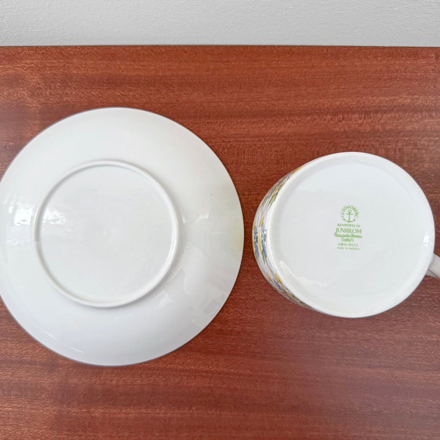 Gustavsberg Juniblom Tea Cup with Saucer showing the underside with green maker’s mark on white ceramic, placed on a wooden surface.