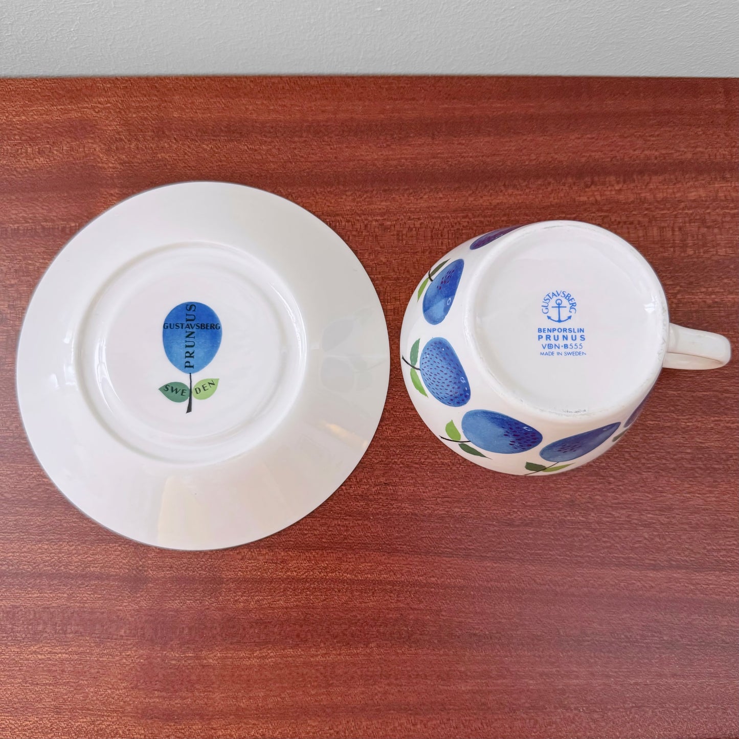 Gustavsberg Prunus Tea Cup with Saucer showing blue fruit pattern with maker’s marks on bottom, vintage Nordic ceramic drinkware designed by Stig Lindberg.