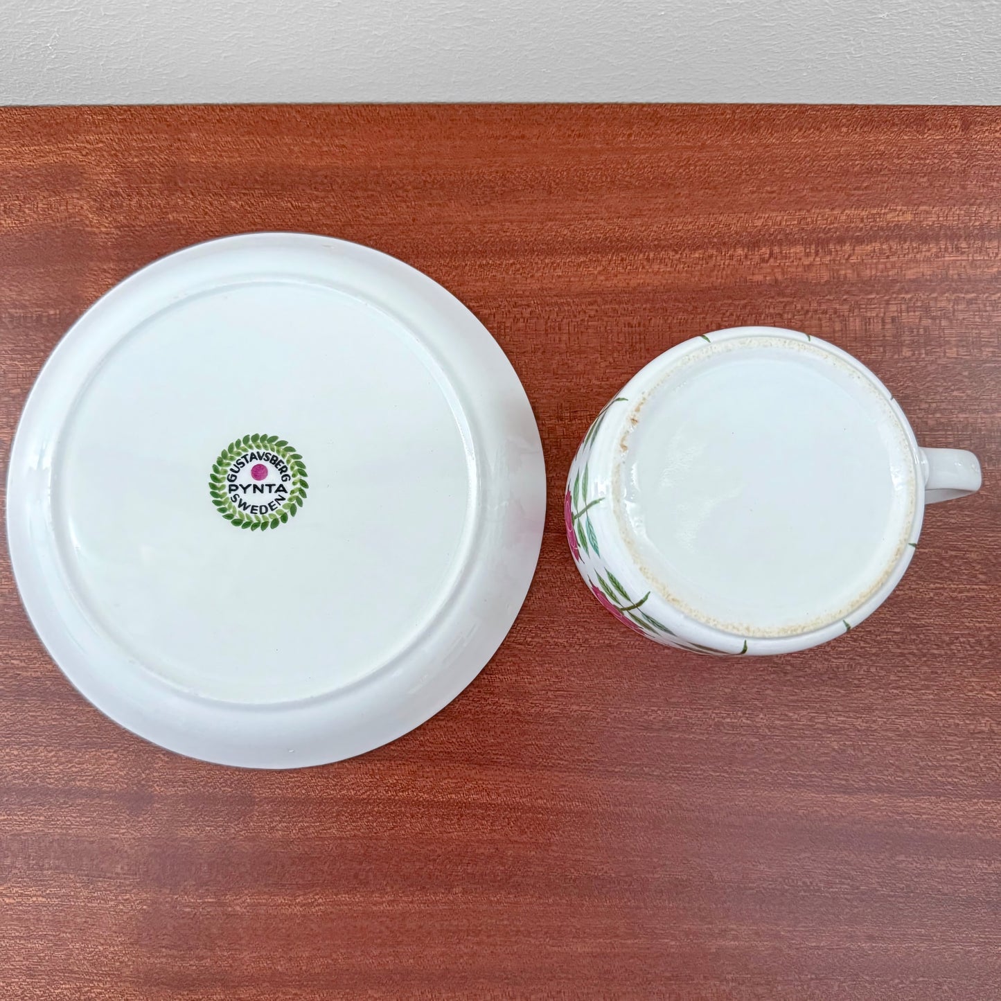 Gustavsberg Pynta Tea Cup with Saucer shown from above, featuring the vintage maker's mark and signs of use on the white ceramic surfaces with subtle decorative accents.