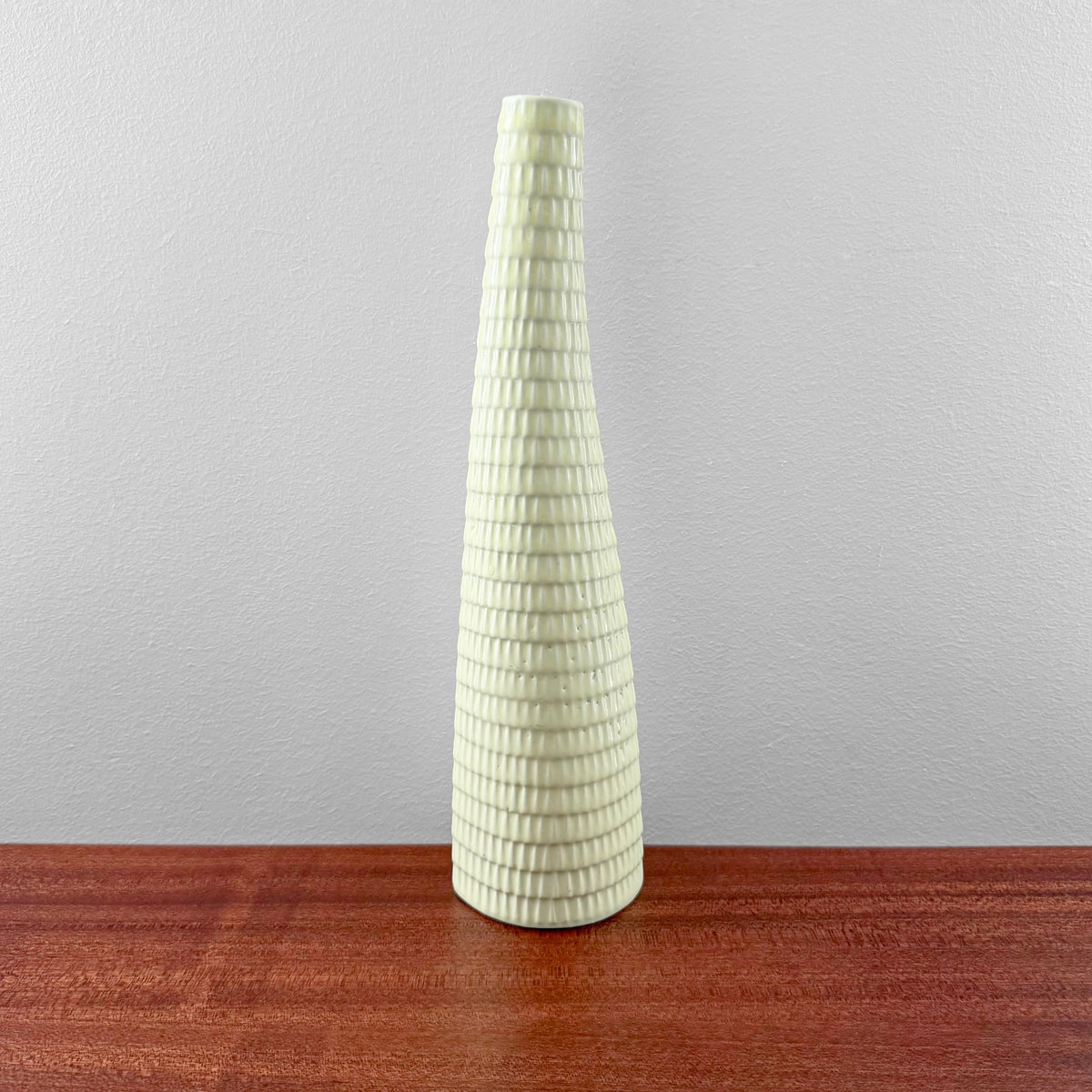 Tall ceramic Gustavsberg Reptil Yellow Vase with textured pattern designed by Stig Lindberg, displayed on a wooden surface against a plain light gray wall.