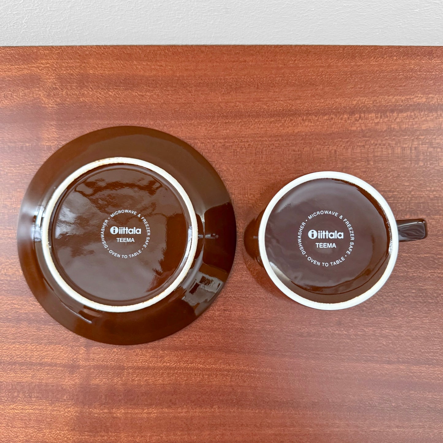 Iittala Teema Brown Tea Cup with Saucer shown from above, featuring dark brown ceramic with white rings and Nordic design markings on wooden surface.