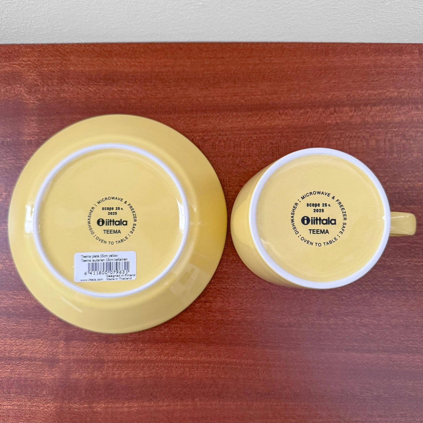 Bottom view of Iittala Teema Yellow Tea Cup with Saucer showing the yellow ceramic finish and printed brand markings on a wooden surface.