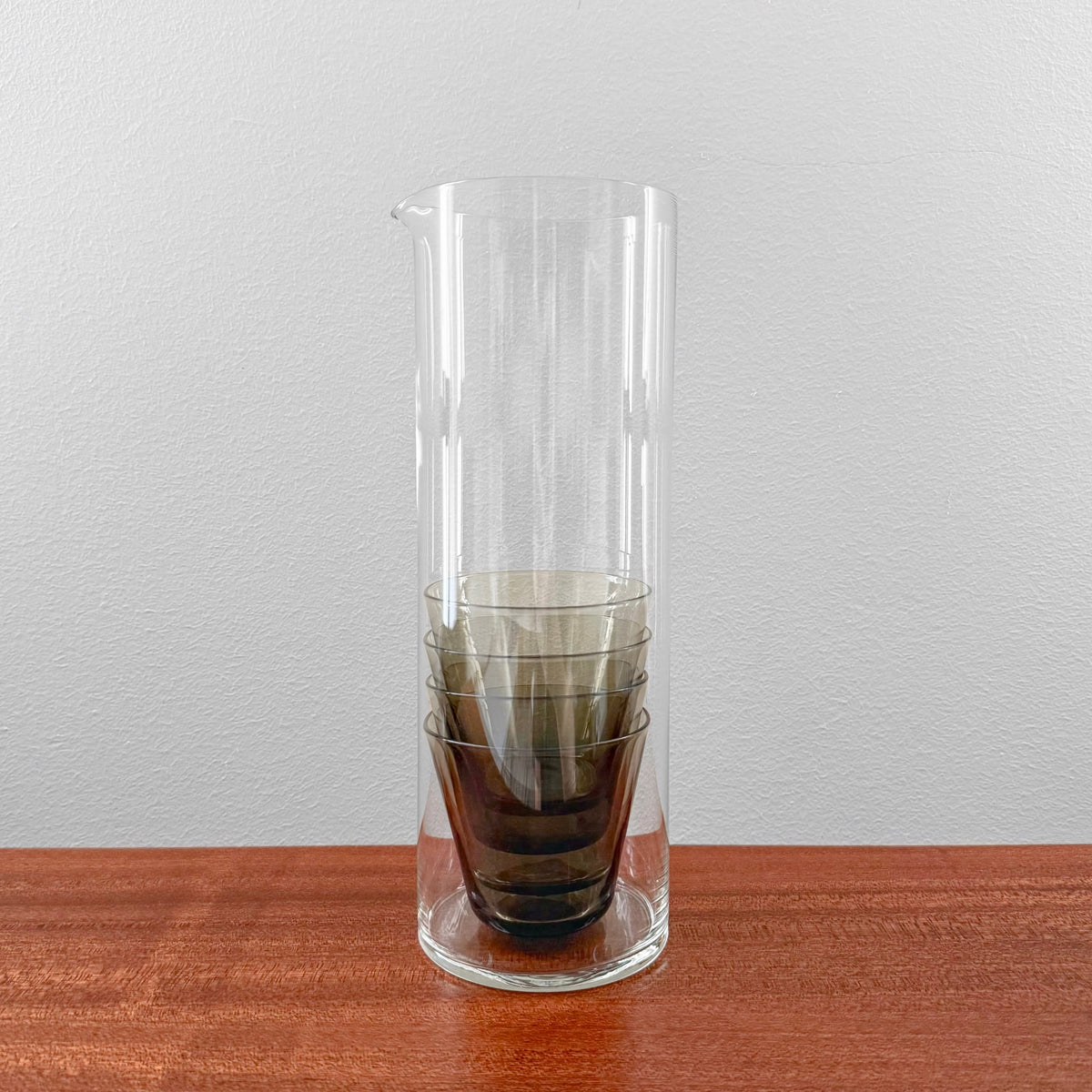 Kaj Franck 1609 Pitcher and Kimara Tumbler Set featuring a clear glass pitcher with four stacked grey glass tumblers, showcasing vintage Nordic glassware craftsmanship.