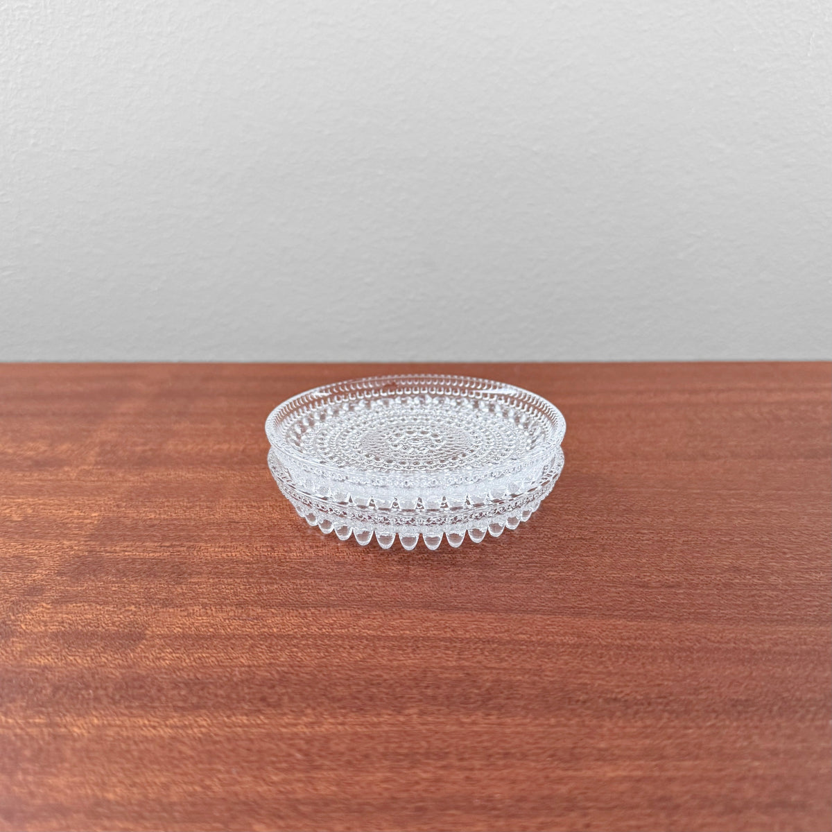 Oiva Toikka Kastehelmi Clear Glass Coasters arranged on a wooden surface, featuring intricate raised bead patterns characteristic of Nordic glassware design.