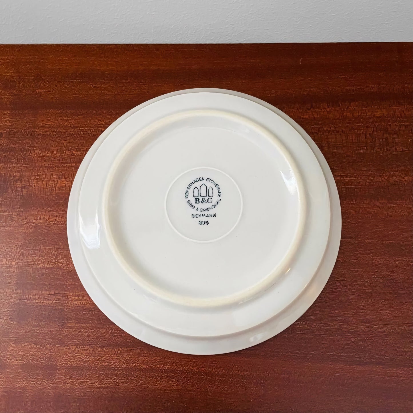 Back view of the cake plate from the Quistgaard Cordial Palet Off-White Tea Cup Trio Set showing the vintage Bing & Grøndahl maker’s mark on a wooden surface.